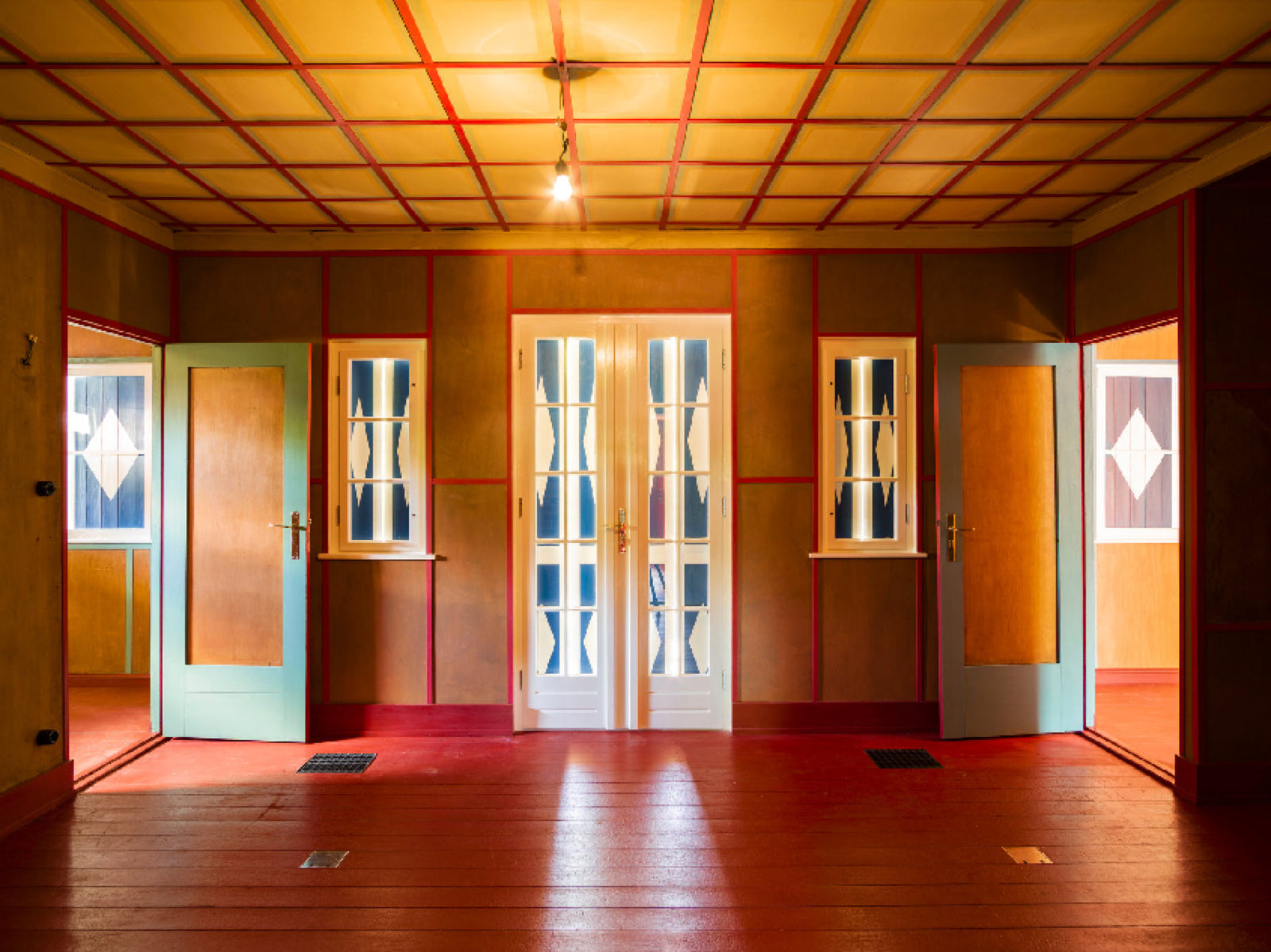 Fine art photography by André Wagner: An empty room contains a gridded wooden ceiling, reddish floorboards and pale door and window openings — Alexander haus #5, Deutschland.