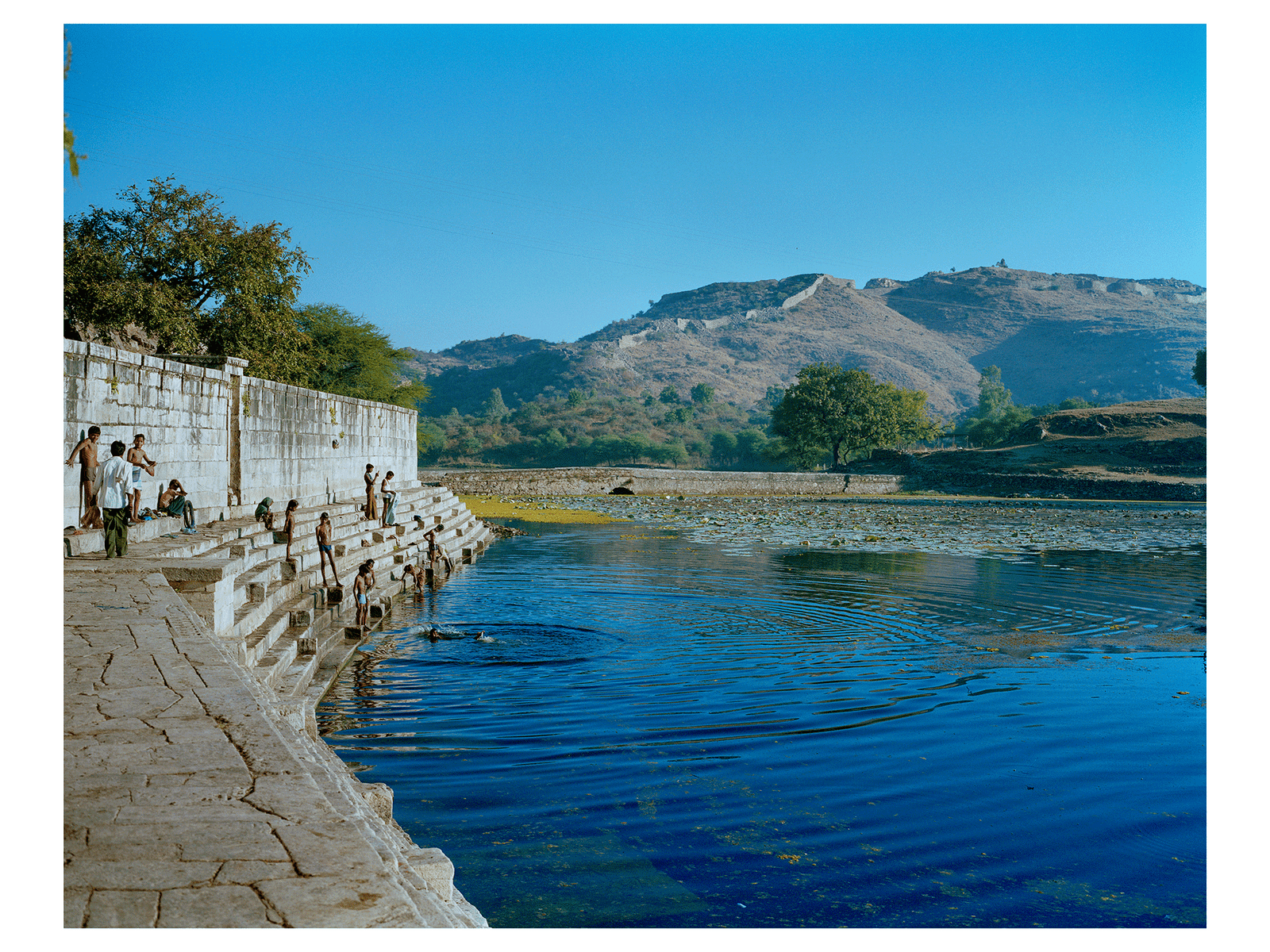 Fine art photography by André Wagner: A stone embankment leads from the lower left into the distance — Am kund des eklingeswar-shiva-tempels in rajasthan, Indien.