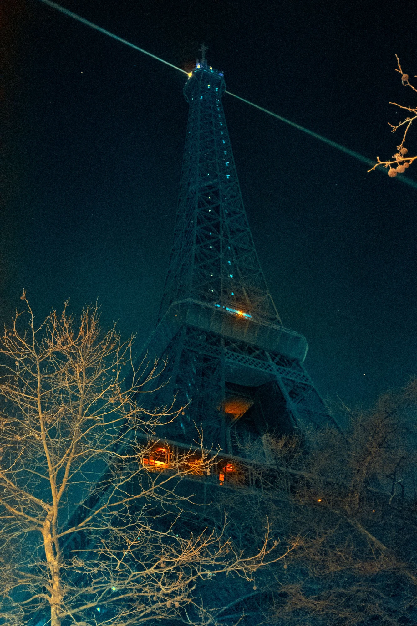 Photographie d’art infrarouge d’André Wagner: La tour Eiffel s’élève comme une structure sombre et bleutée dans un format vertical presque noir — Amour en Paris: The Romance of the Eiffel Tower.