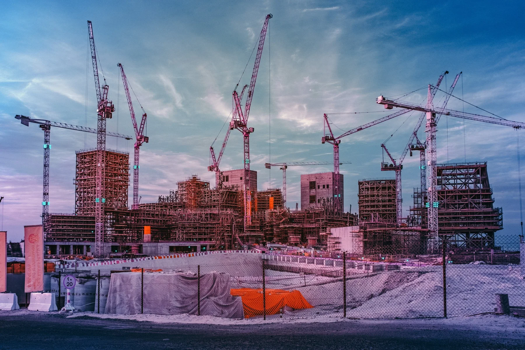 Construction site with several cranes and steel frameworks at sunset, construction site under construction.