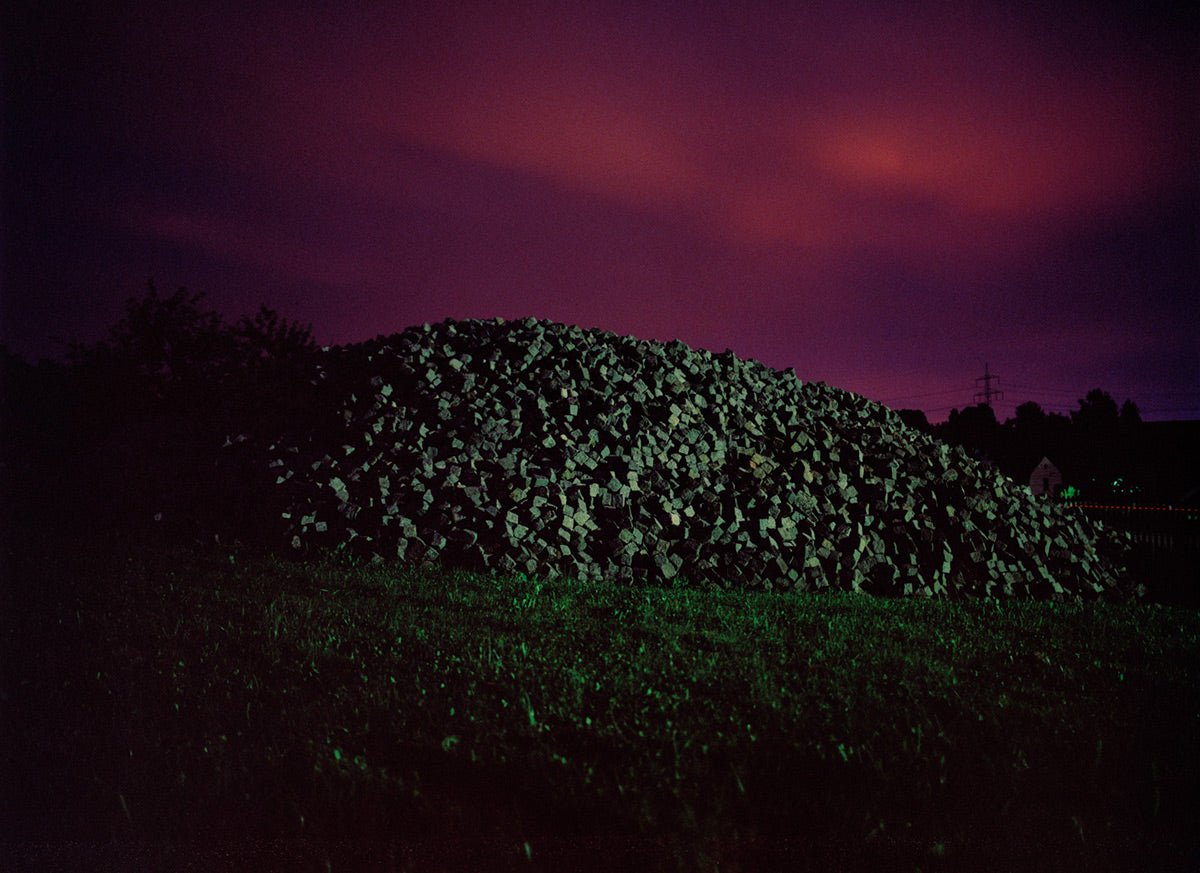 Photographie d’art d’André Wagner: Un amas allongé de pierres anguleuses repose sous un ciel rouge sombre — Behind the Cobbles, Deutschland.