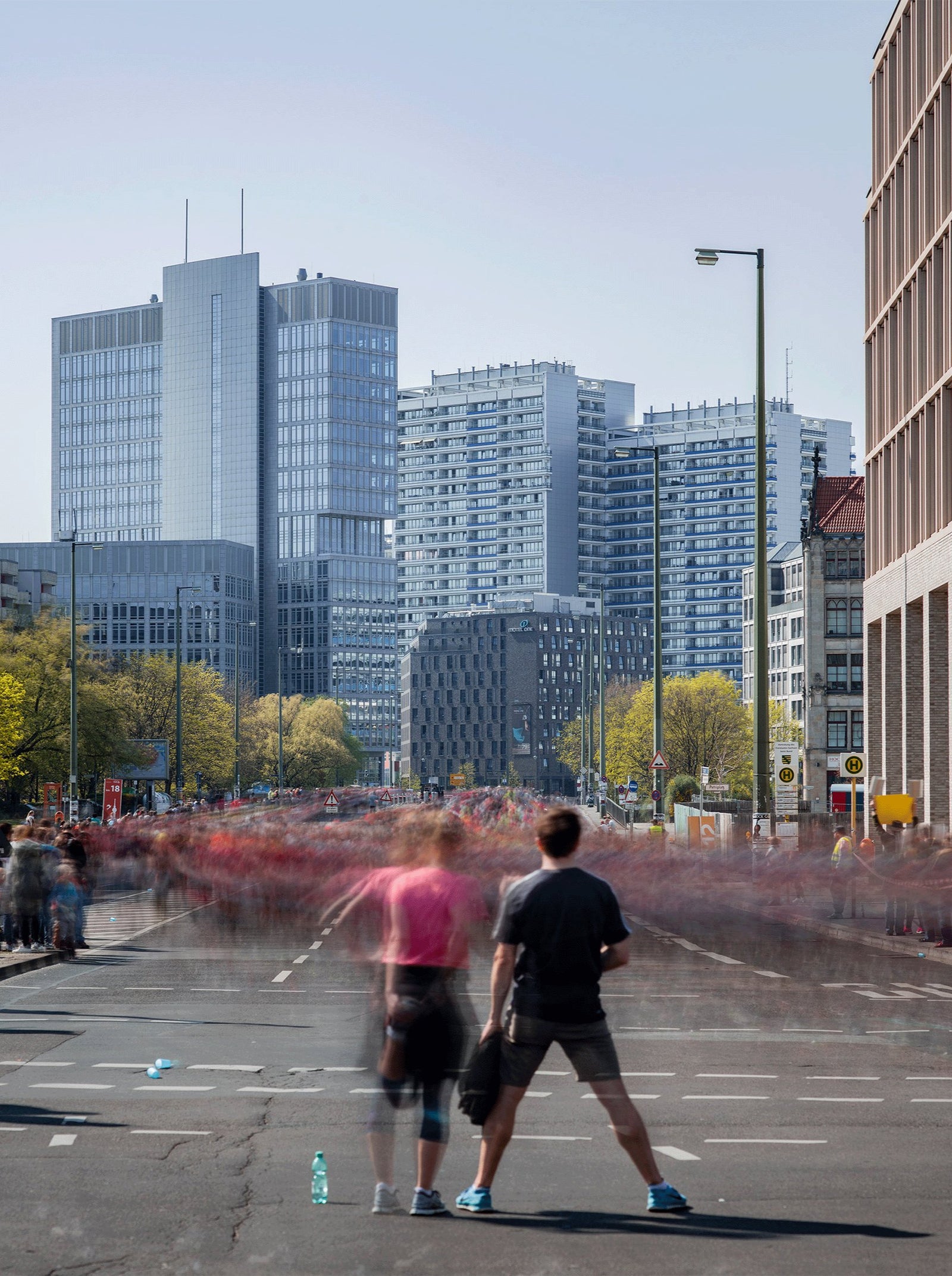 Photographie d’art d’André Wagner: Deux personnes se tiennent au premier plan d’une large rue — Berlin half marathon, Leipziger strasse ii, Deutschland.