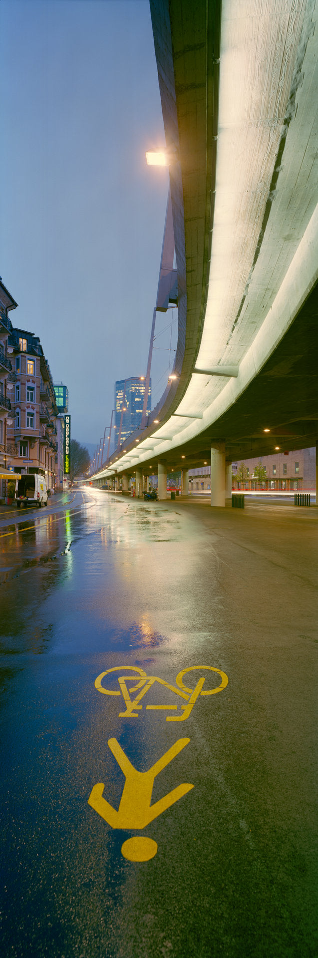 Fine art photography by André Wagner: A yellow bicycle symbol and arrow occupy wet, dark blue paving — Bicycle Path.