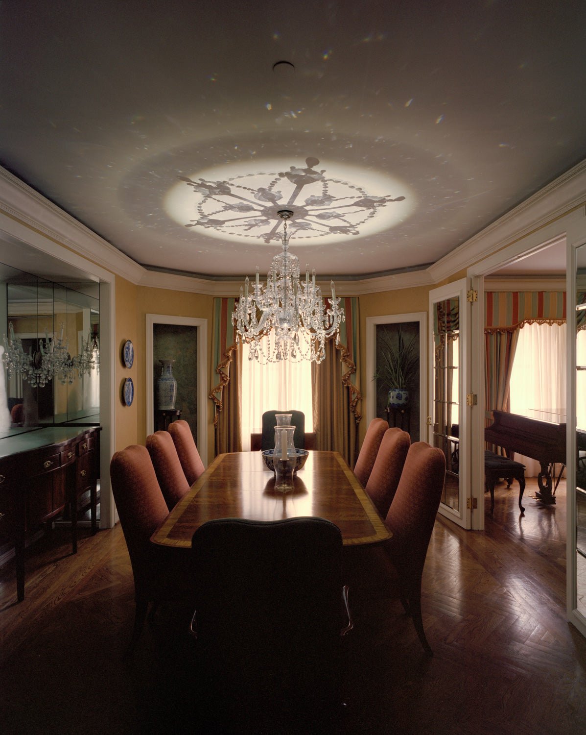 Photographie d’art d’André Wagner: Un lustre de verre est suspendu au-dessus d’une longue table à manger — Ceiling Crystal, USA.