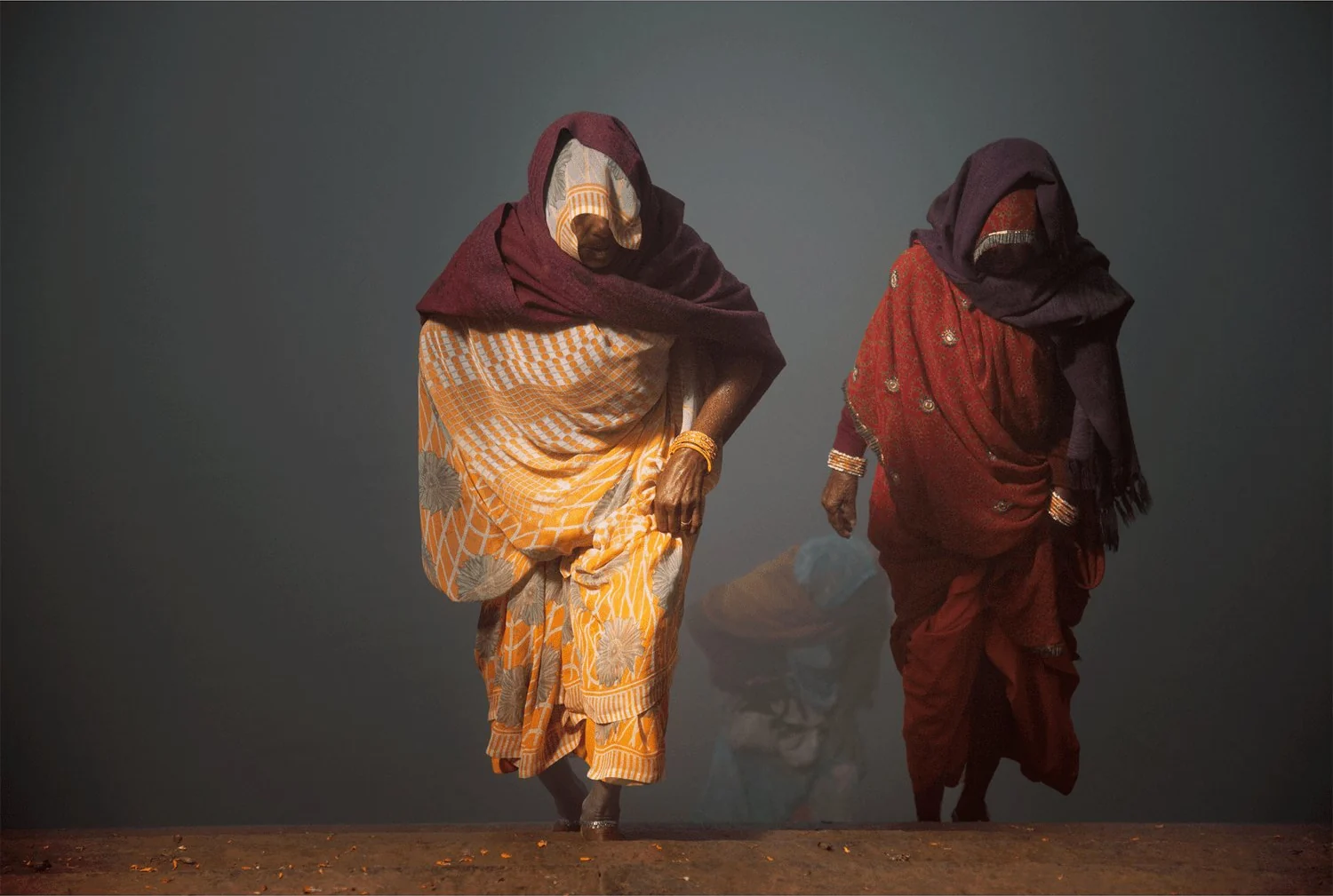 Fotokunst von Andr&eacute; Wagner: Zwei Frauen treten deutlich aus dem grauen Nebel hervor, w&auml;hrend hinter ihnen eine weitere Gestalt nur schwach erkennbar bleibt &mdash; Coming back from yamuna river, Indien.