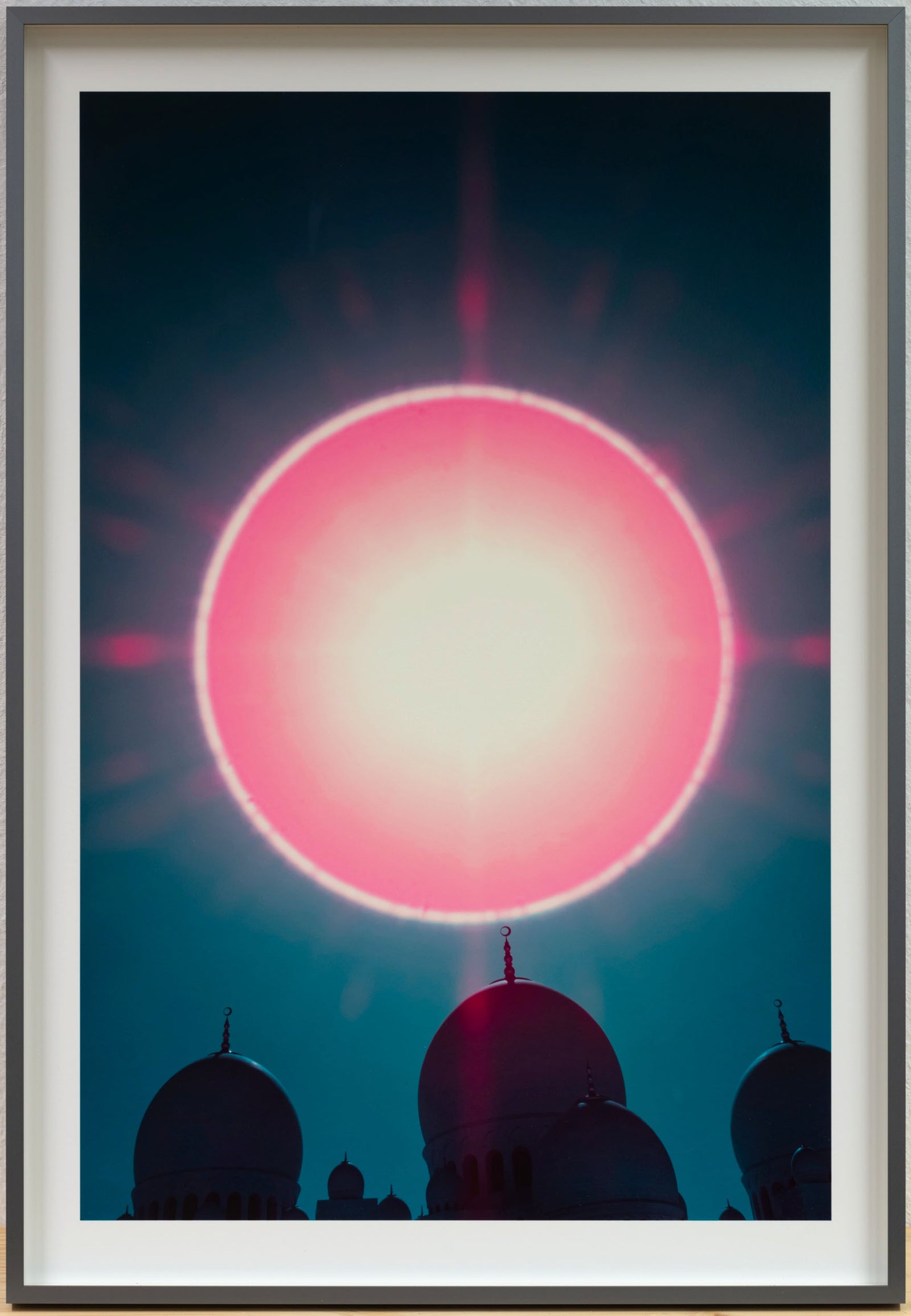 Infrared fine art photography by André Wagner: A large pink-red circle stands above dark dome silhouettes — Cosmic crown: over the sheikh zayed grand mosque.