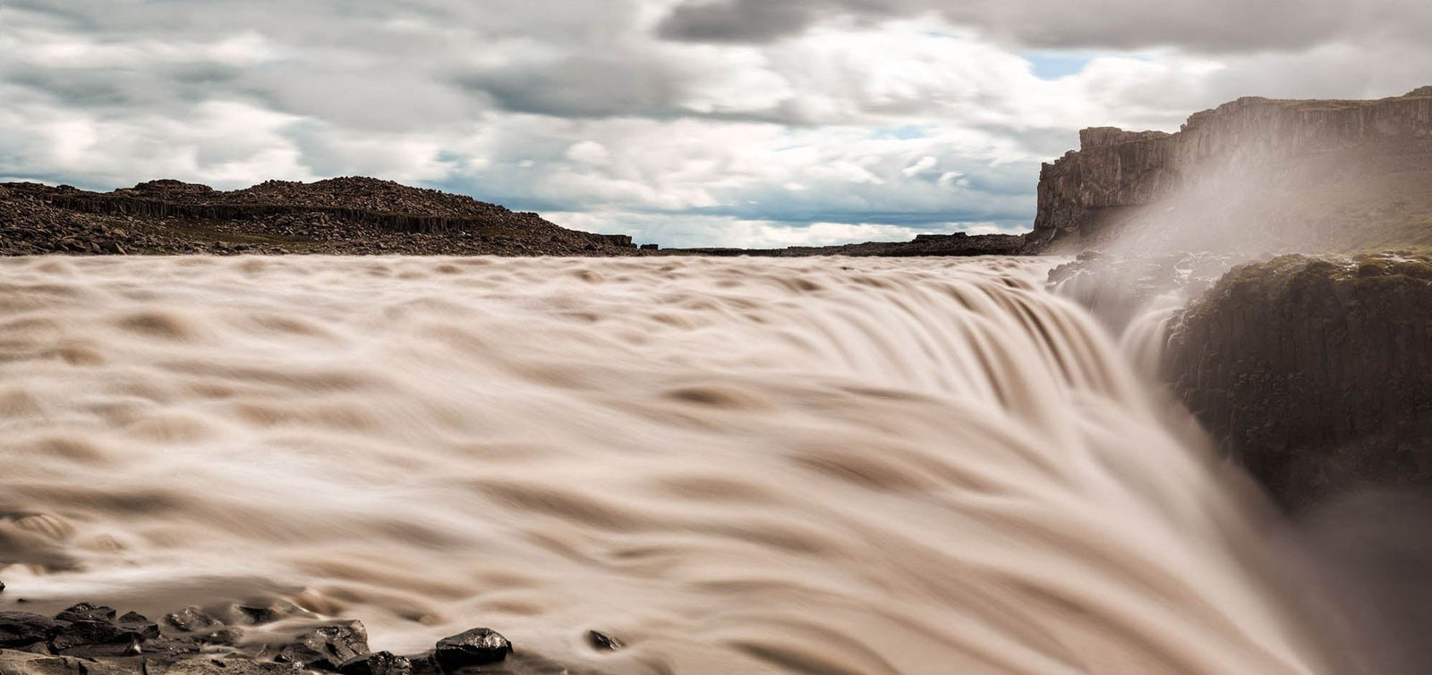 Photographie d’art d’André Wagner: De larges nappes d’eau claire franchissent l’arête rocheuse et disparaissent à droite dans des embruns qui s’élèvent — Dettifoss, Island.