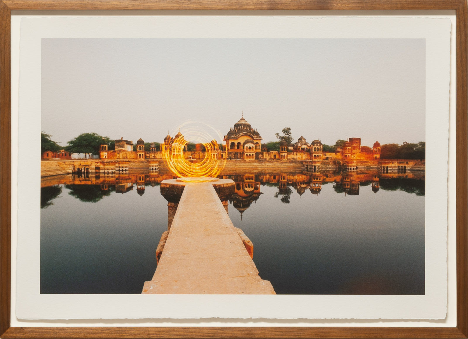 Photographie d’art d’André Wagner: Une passerelle claire traverse en ligne droite une eau sombre vers une architecture éloignée — Dimension door, Indien.
