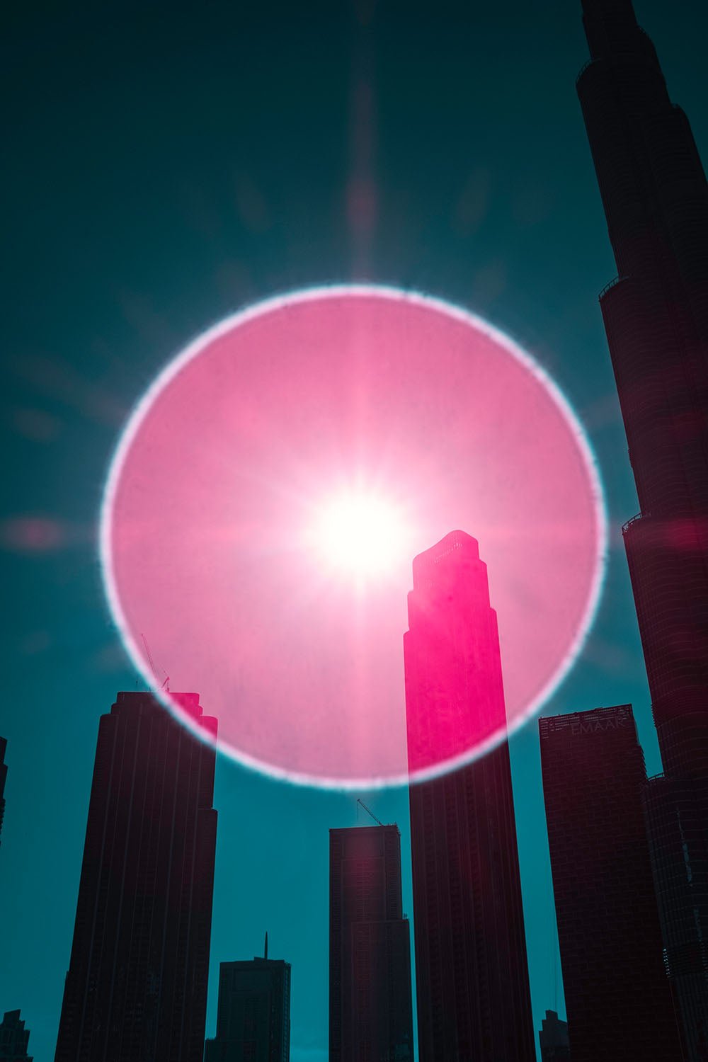 Photographie d’art infrarouge d’André Wagner: Un grand cercle lumineux rose se superpose aux silhouettes sombres de gratte-ciel — Dubai in the Eye of the Cosmic Observer, Vereinigte Arabische Emirate.