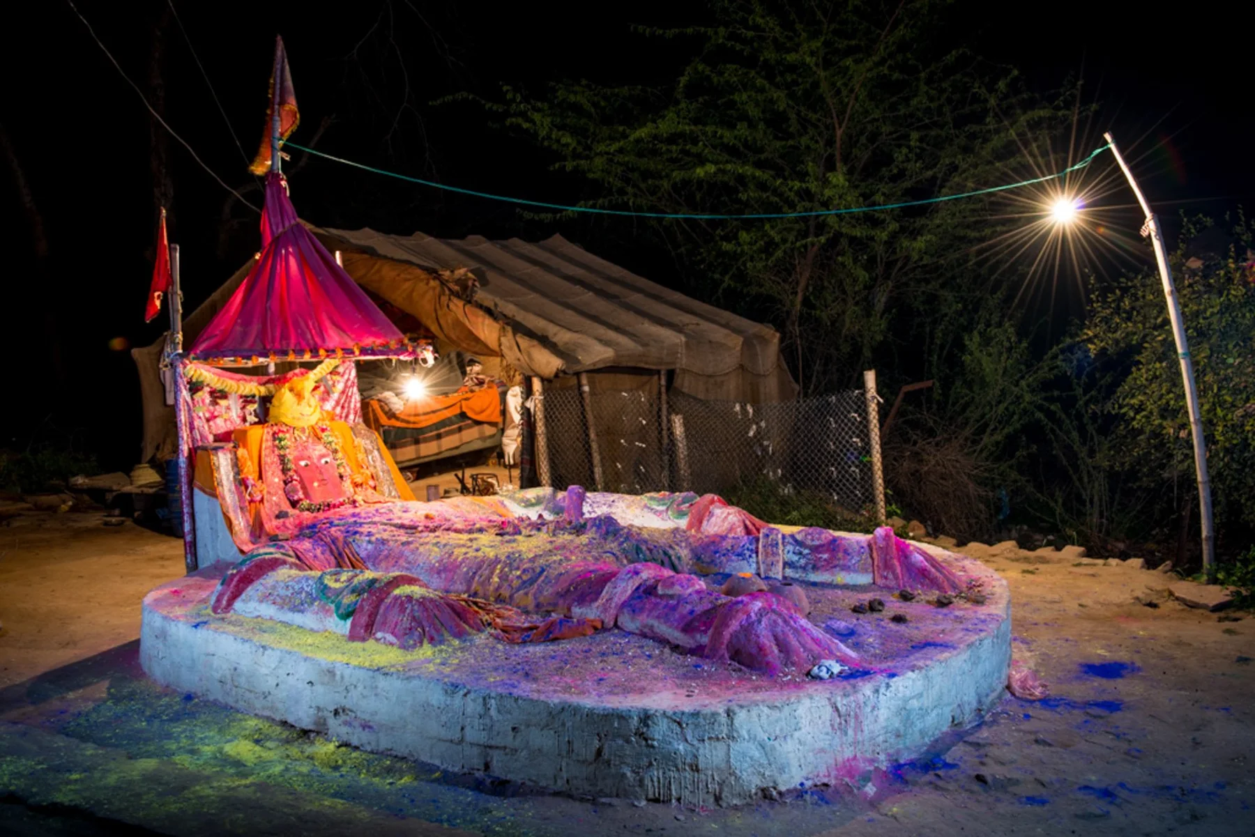 A man in bright clothes and headscarf walks barefoot over a path at night.