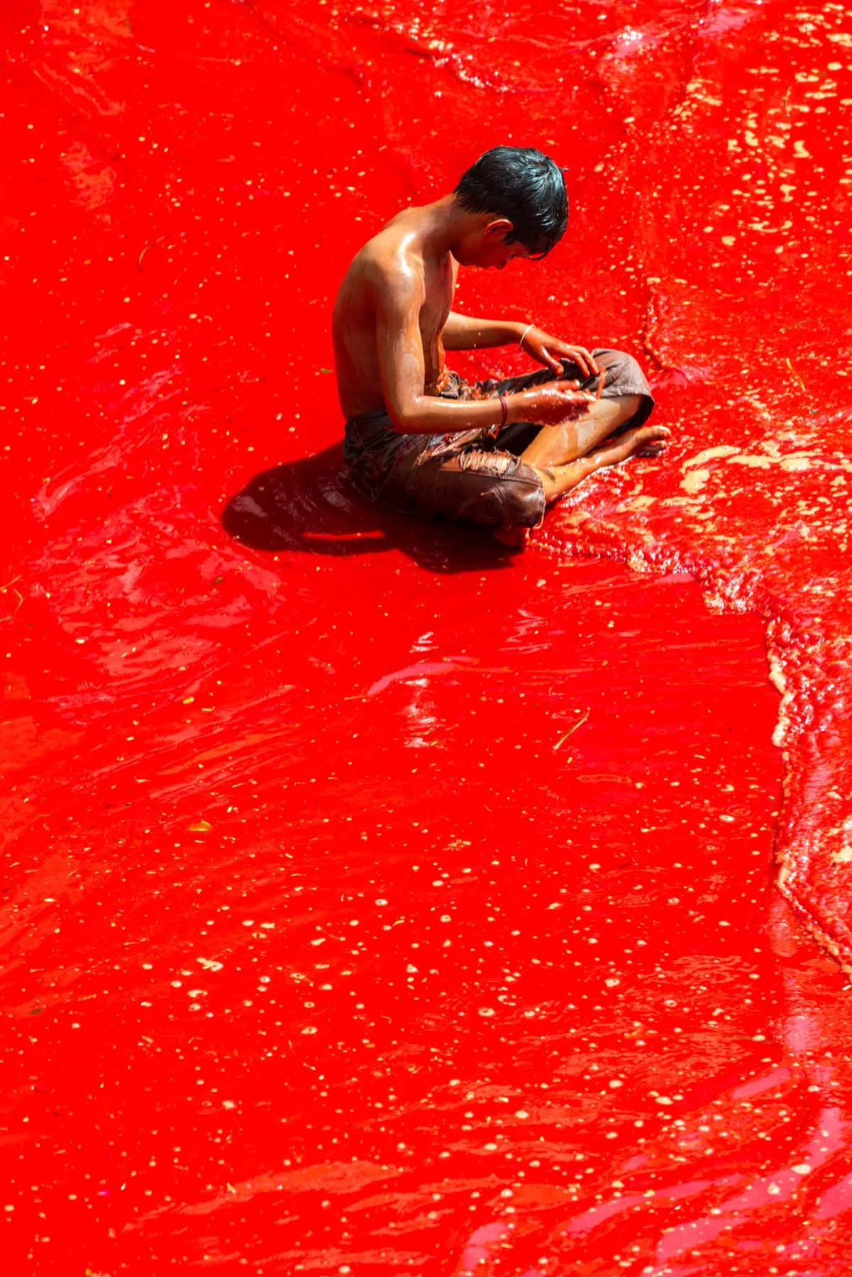 A man sits on an intensely red, wet floor.