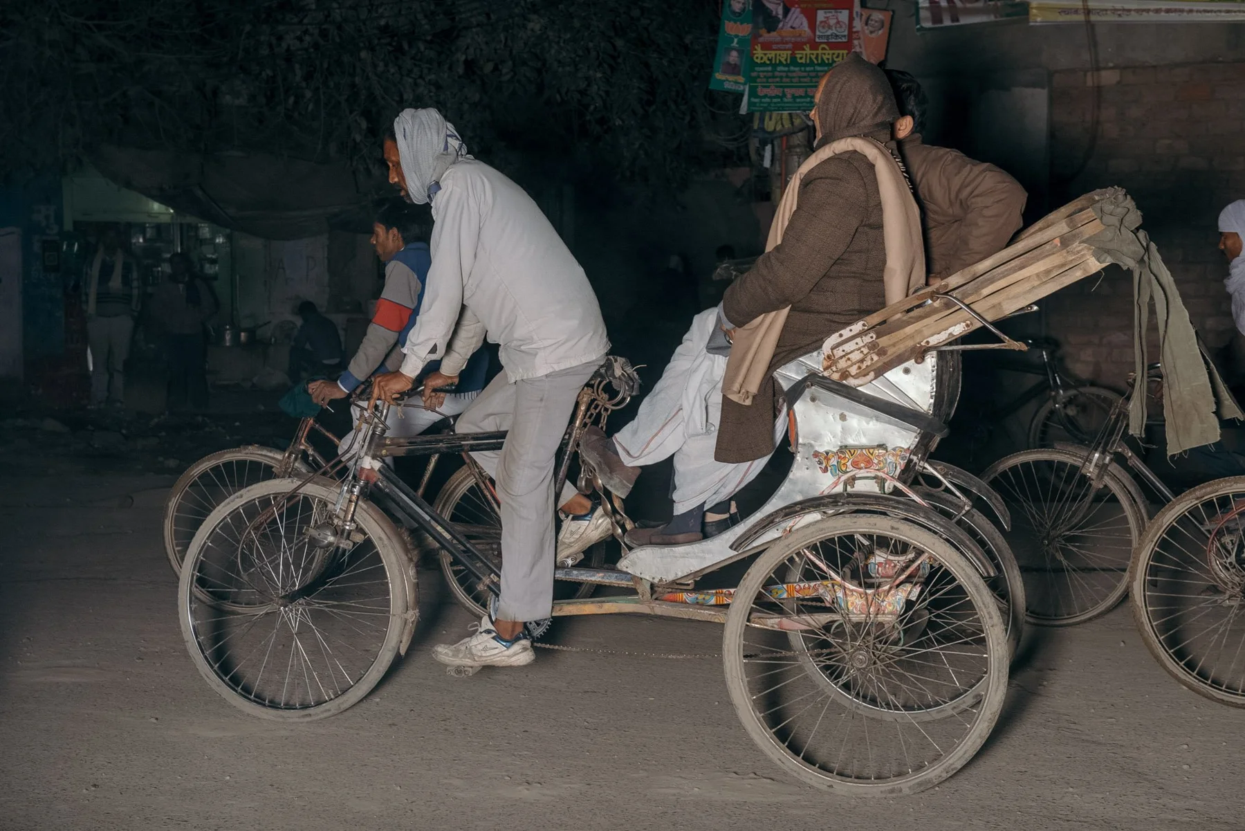 Bicycle rickshaw with driver and passengers on a road at night.