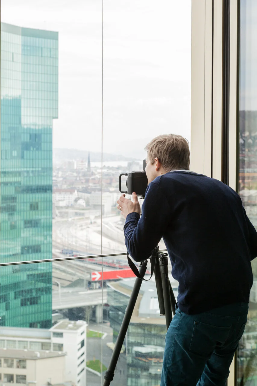 Photographe avec un trépied devant une grande fenêtre donnant sur la ville