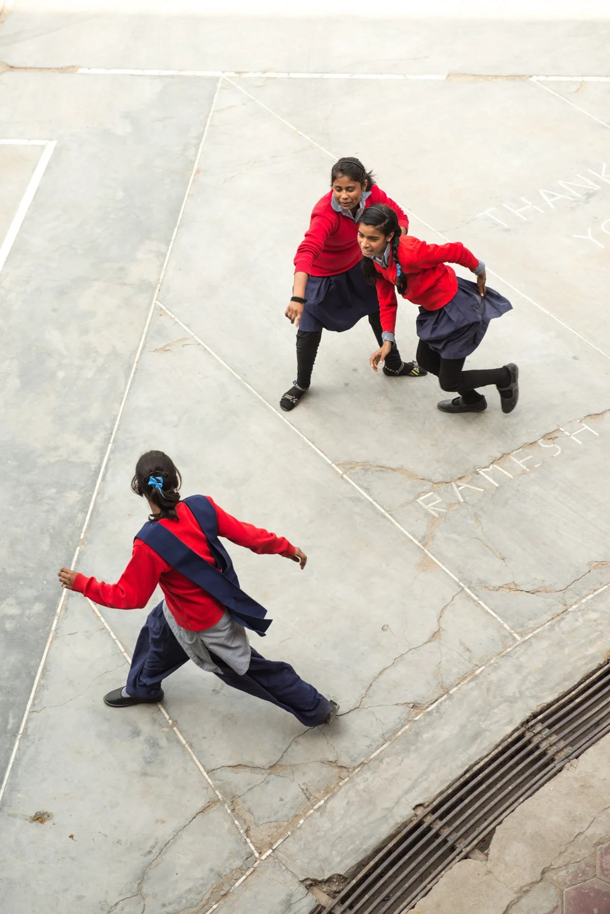 Photograph of people in red tops moving across a pale paved space