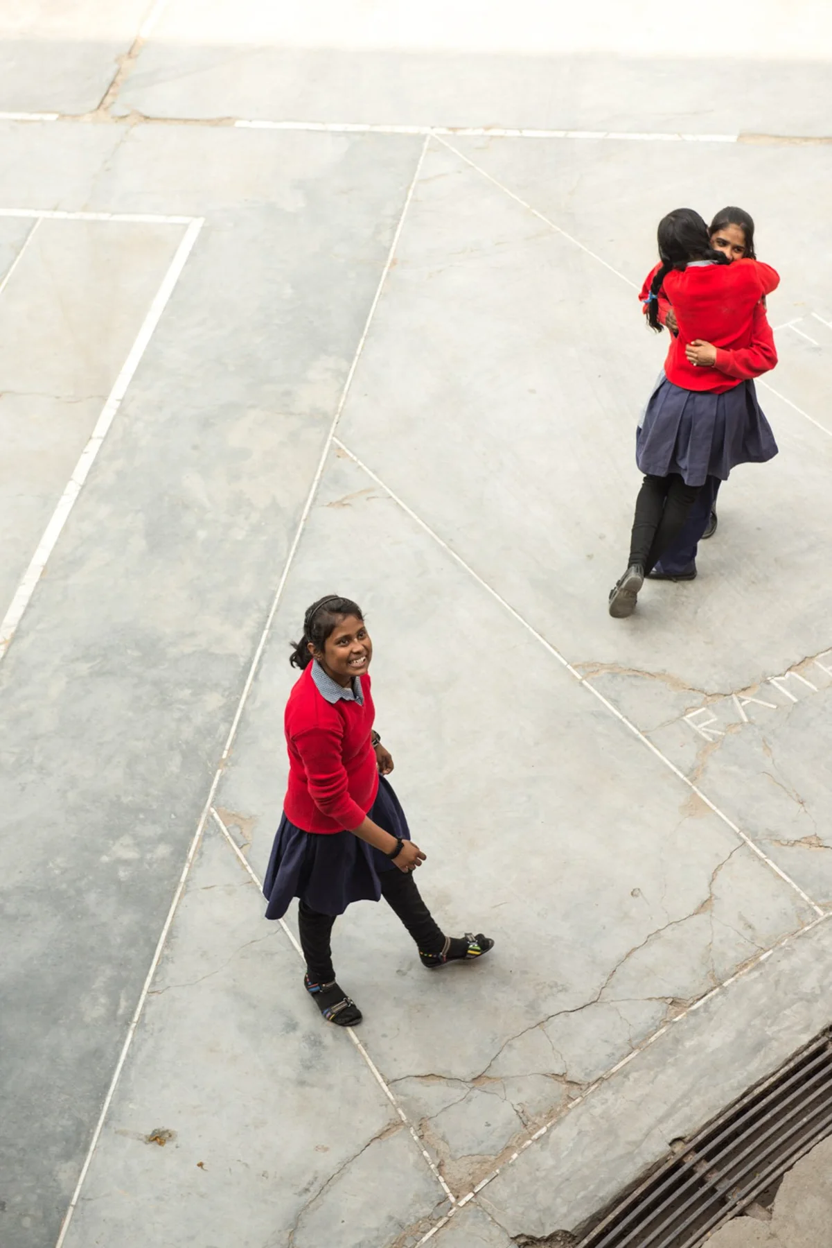 Photograph of two people in red on a pale paved space, seen from above