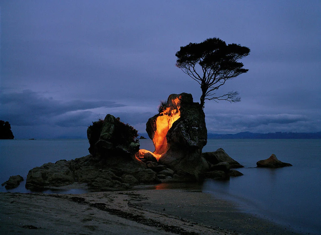 Photographie d’art d’un rocher éclairé et d’un arbre au bord de l’eau au crépuscule