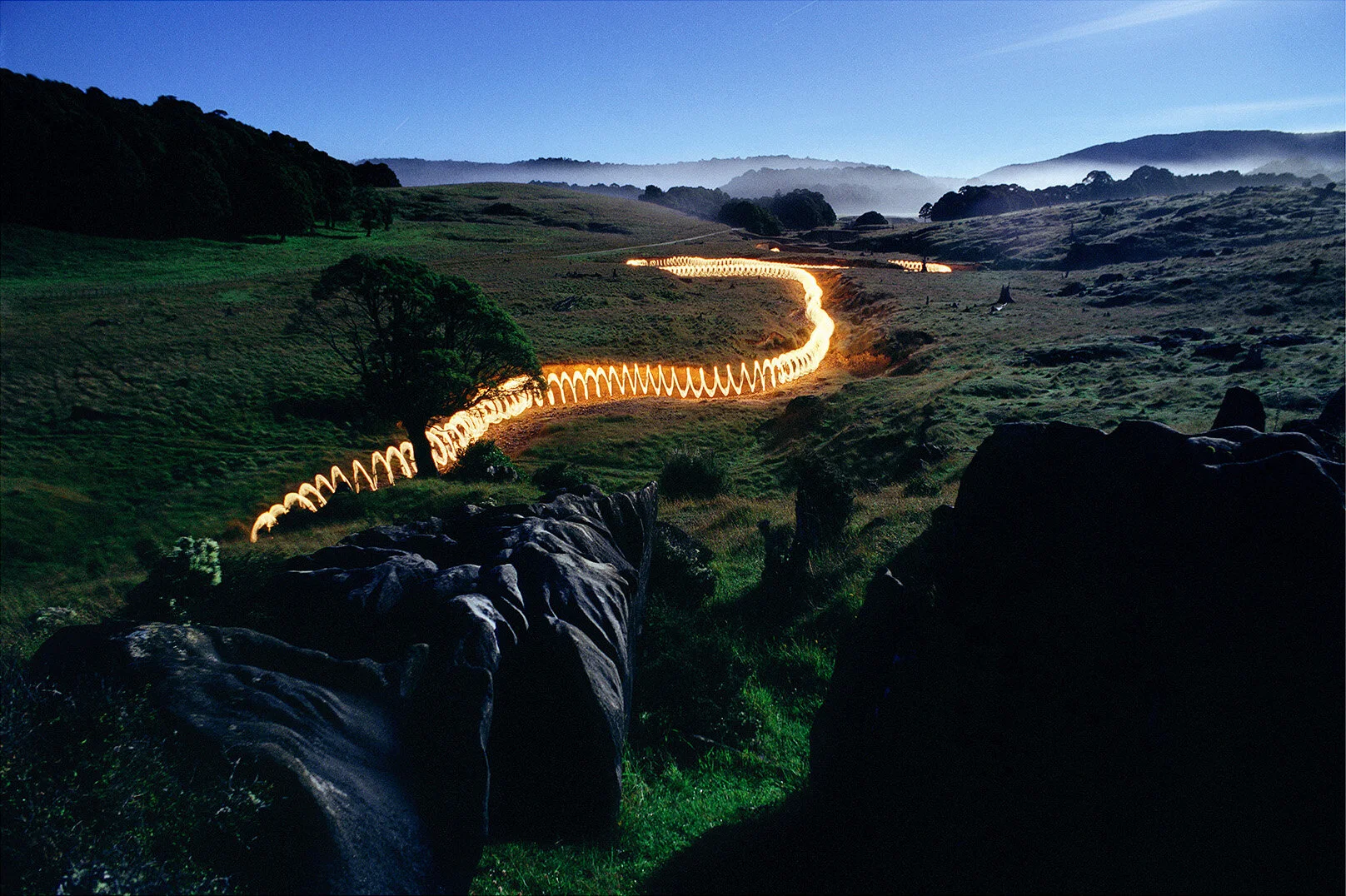Photographie d’art d’une traînée lumineuse sinueuse dans un paysage rocheux nocturne