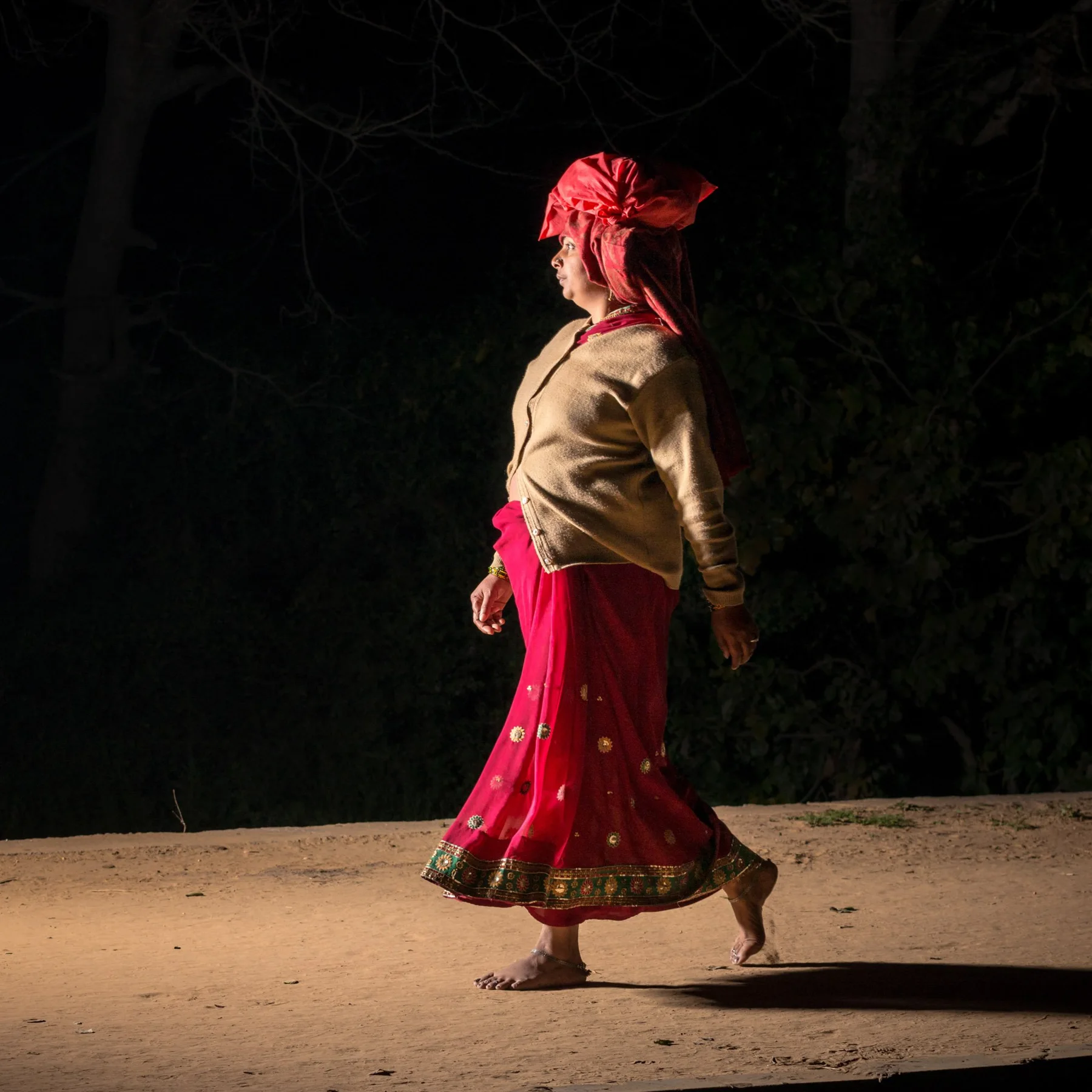 Woman in red skirt and bright cloth on a nightlit street.