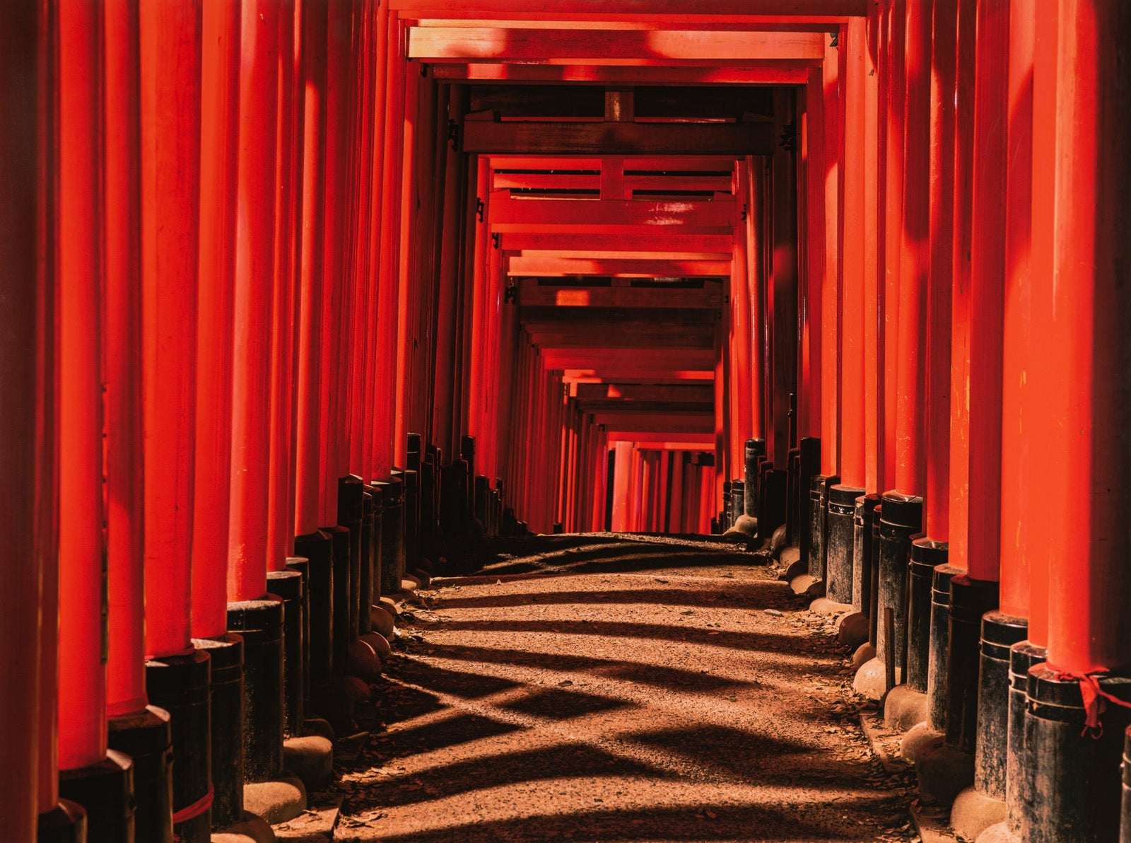 Fine art photography by André Wagner: Strong red gates form a narrow passage whose ground recedes sharply — Fushimi inari taisha 8, Japan.