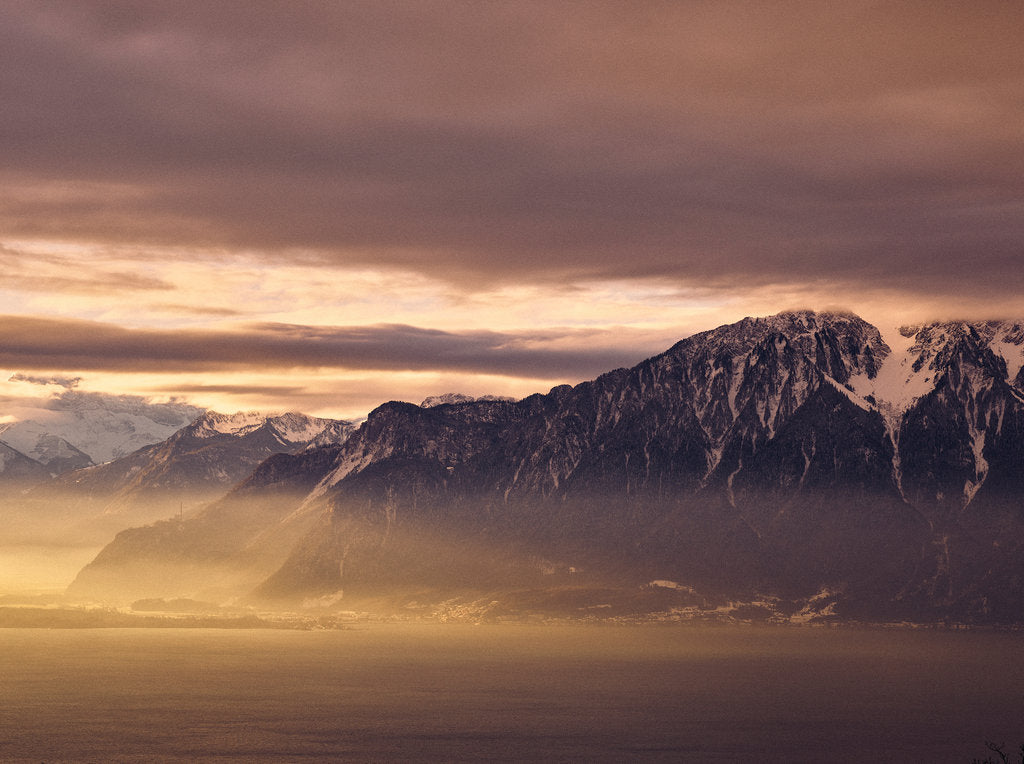 Fine art photography by André Wagner: A dark mountain mass rises above similarly toned water — Genfer See.