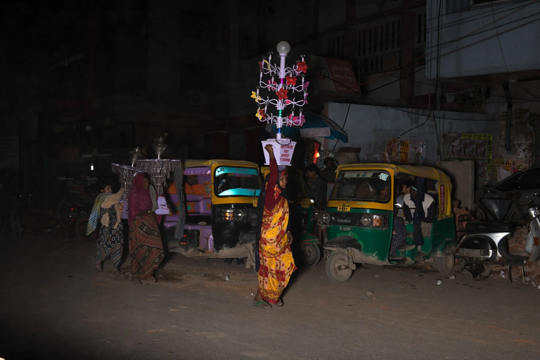 Decorated construction on a nightly road between people and car ikshas.