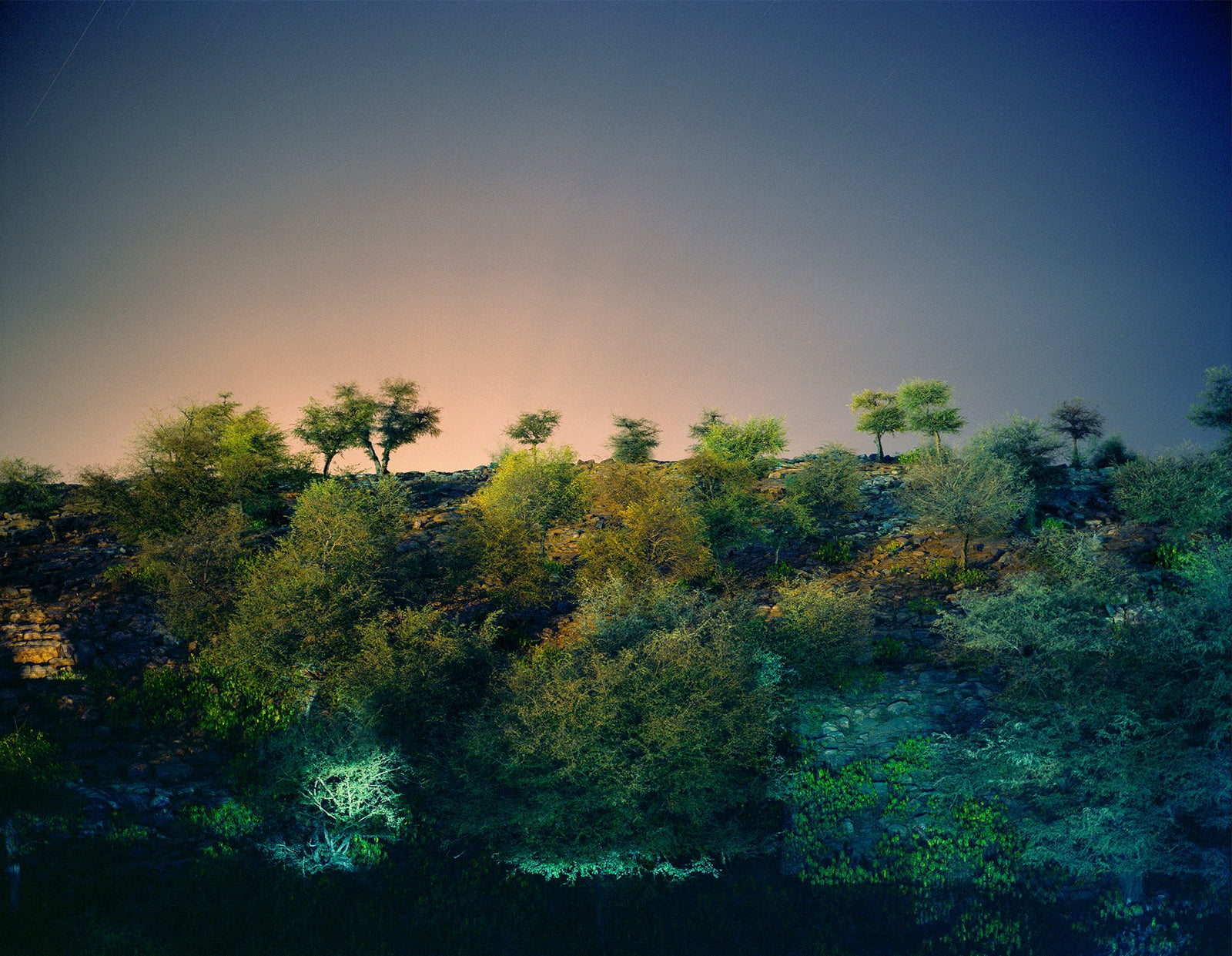Photographie d’art d’André Wagner: Une colline basse et végétalisée se détache sur un ciel qui passe d’un horizon chaud à un bleu profond — Govardhan hill, Indien.