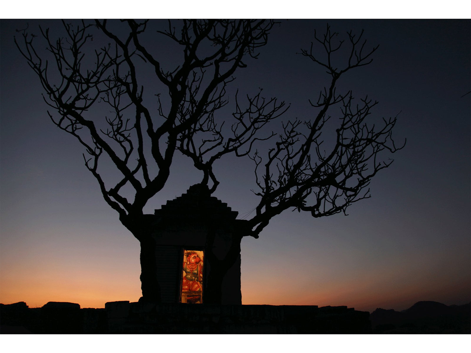 Fine art photography by André Wagner: A small dark temple stands before the last warm strip on the horizon — Hanuman temple, Indien.