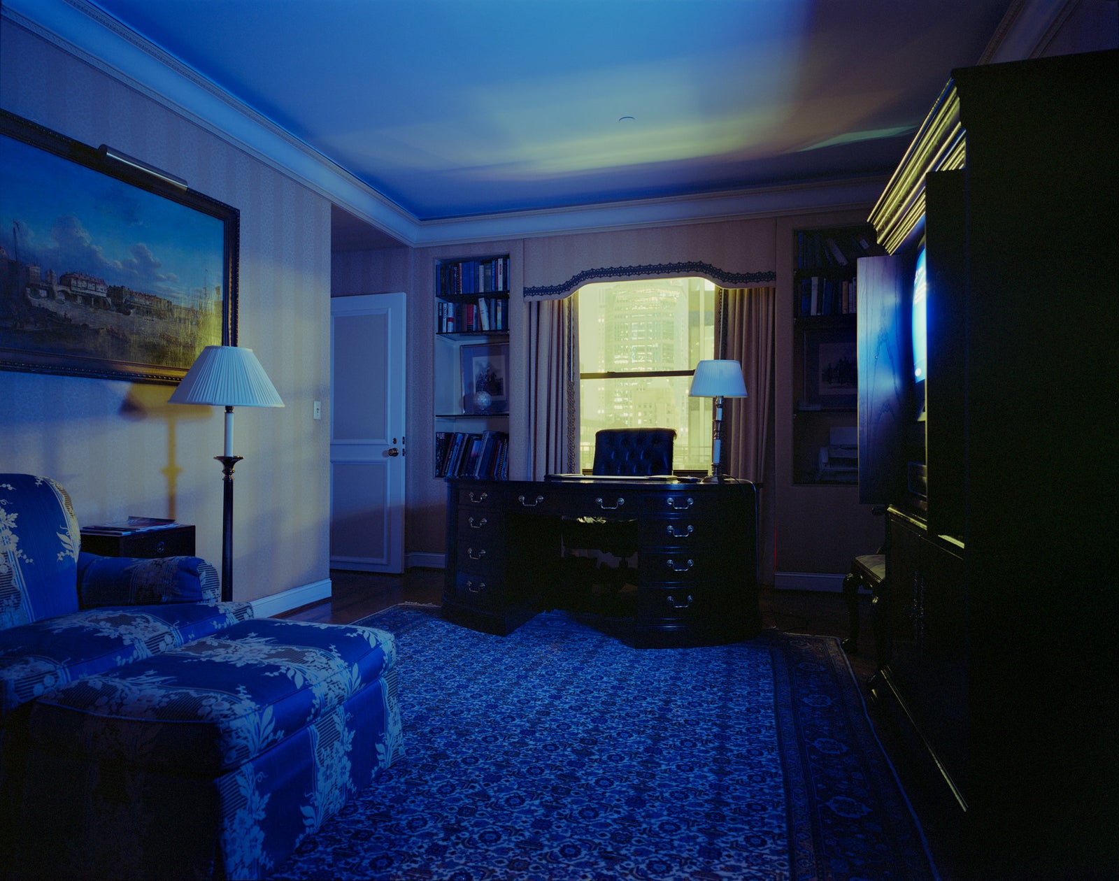 Fine art photography by André Wagner: A dark sofa and floor lamp occupy the left, while a bright window opens the rear — Hotel Room in New York 3.