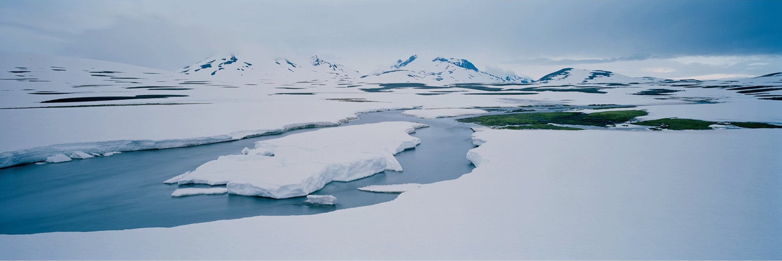 Photographie d’art d’André Wagner: Un cours d’eau bleu serpente dans un paysage en grande partie blanc — Island spring, Island.