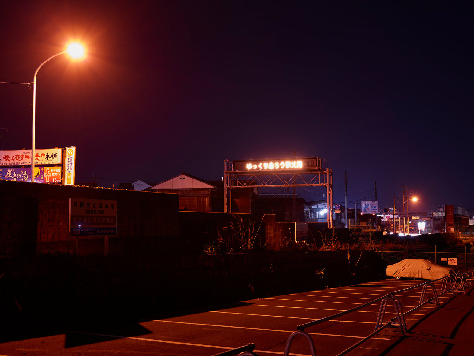 Fine art photography by André Wagner: A curved street lamp burns orange above a dark street — Japan Street.