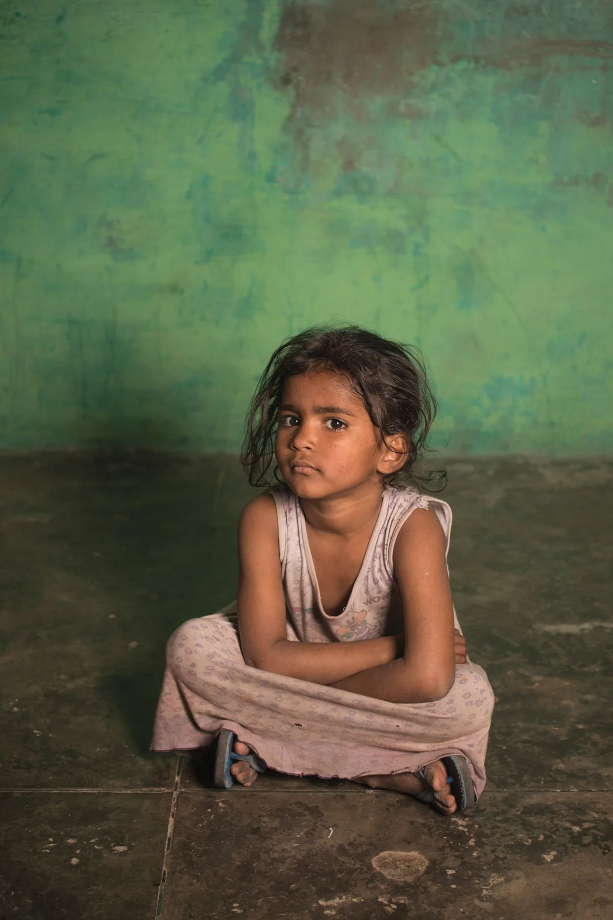 The child sits with his legs angled in front of a green wall.