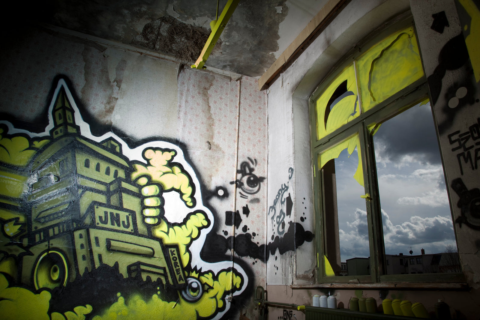 Photographie d’art d’André Wagner: Un dessin mural jaune et vert, cerné de noir, occupe la gauche d’un intérieur brut — Korea Spray.