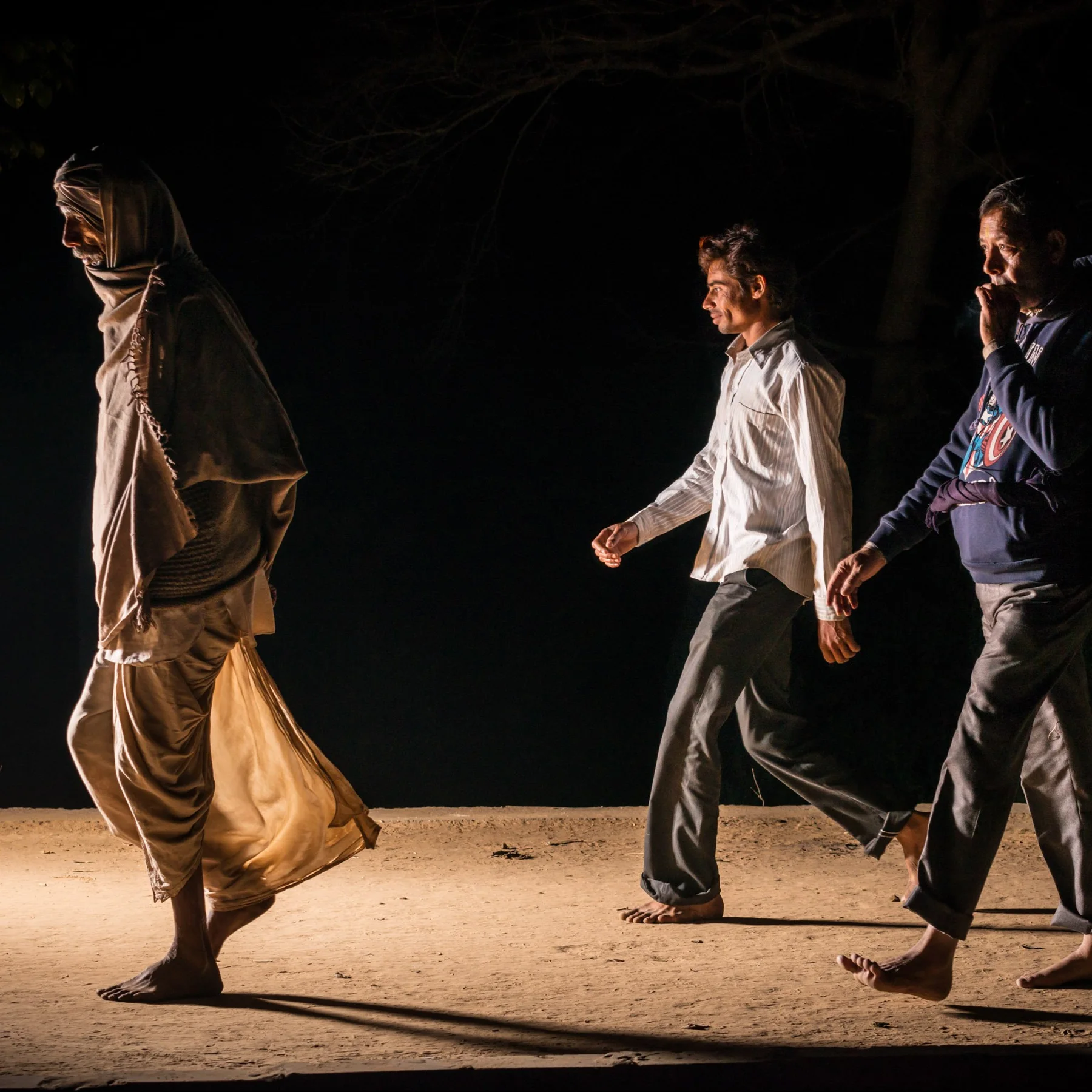 Men walk across a dark road in the side light.
