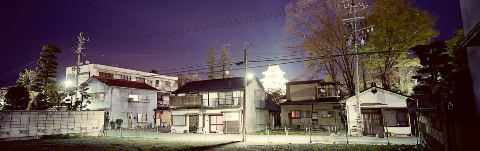 Photographie d’art d’André Wagner: Une rangée de maisons basses se tient sous un ciel nocturne violet — Matsumoto castle 3, Japan.