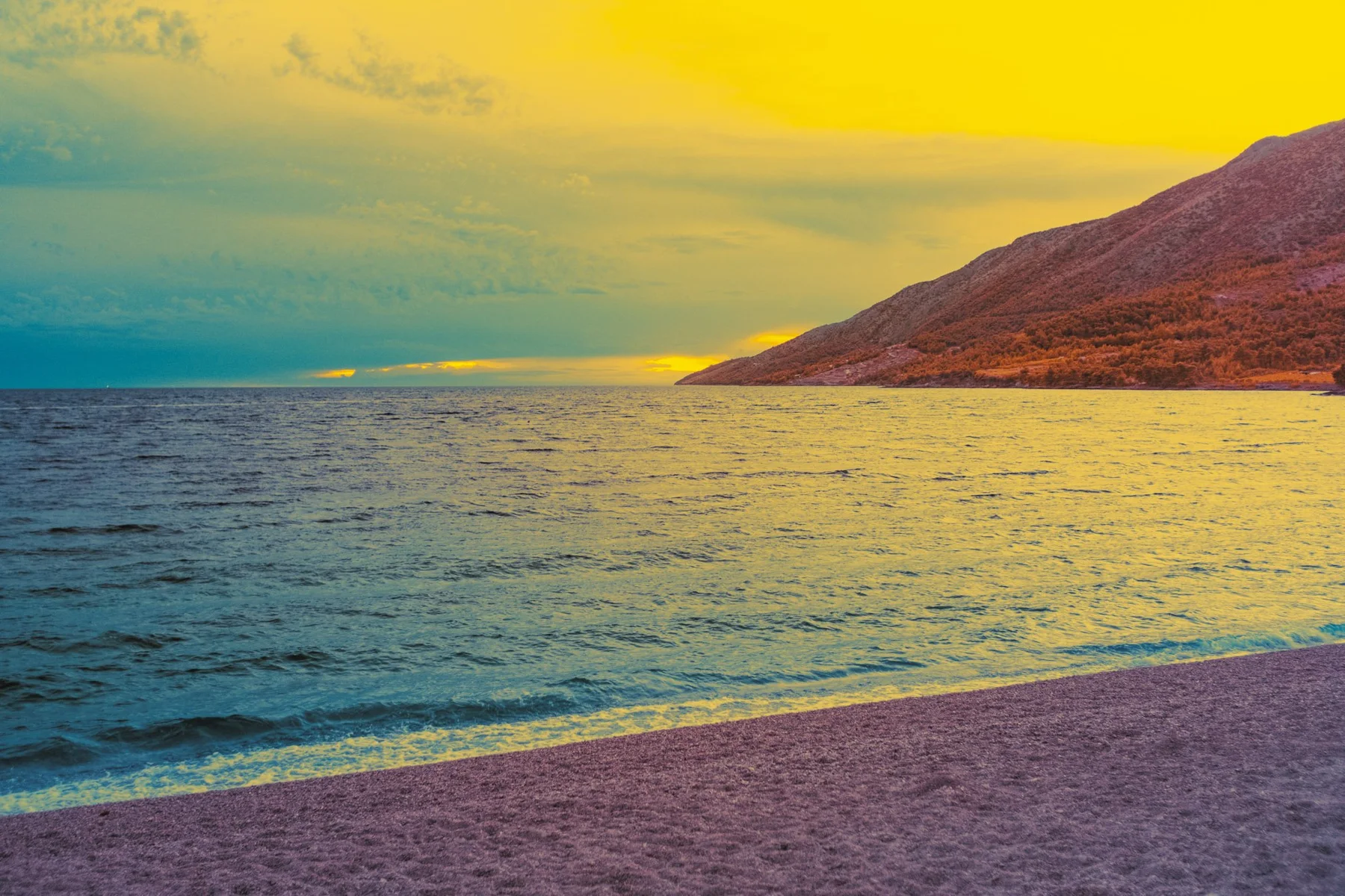 Plage devant un versant montagneux sous un ciel jaune.