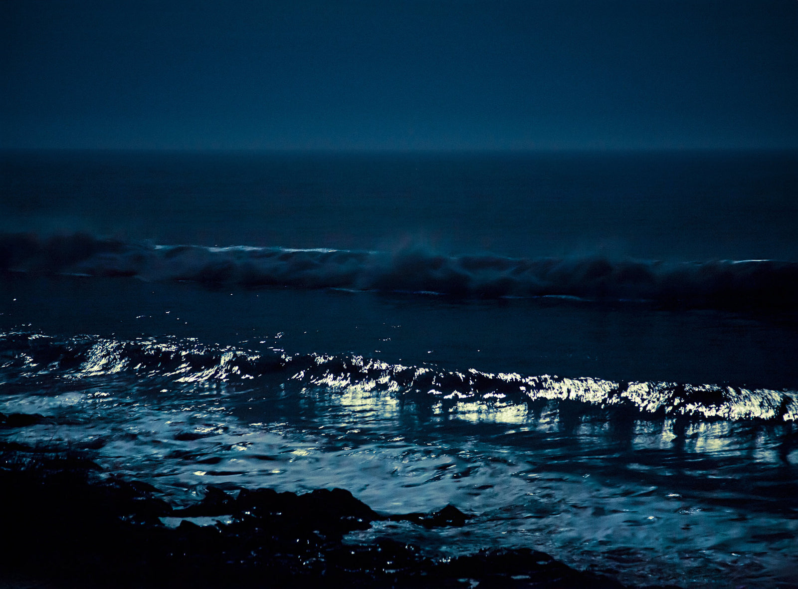 Fine art photography by André Wagner: Silver highlights mark individual wave crests in a dark-blue seascape — Moonwaves 3, Portugal.
