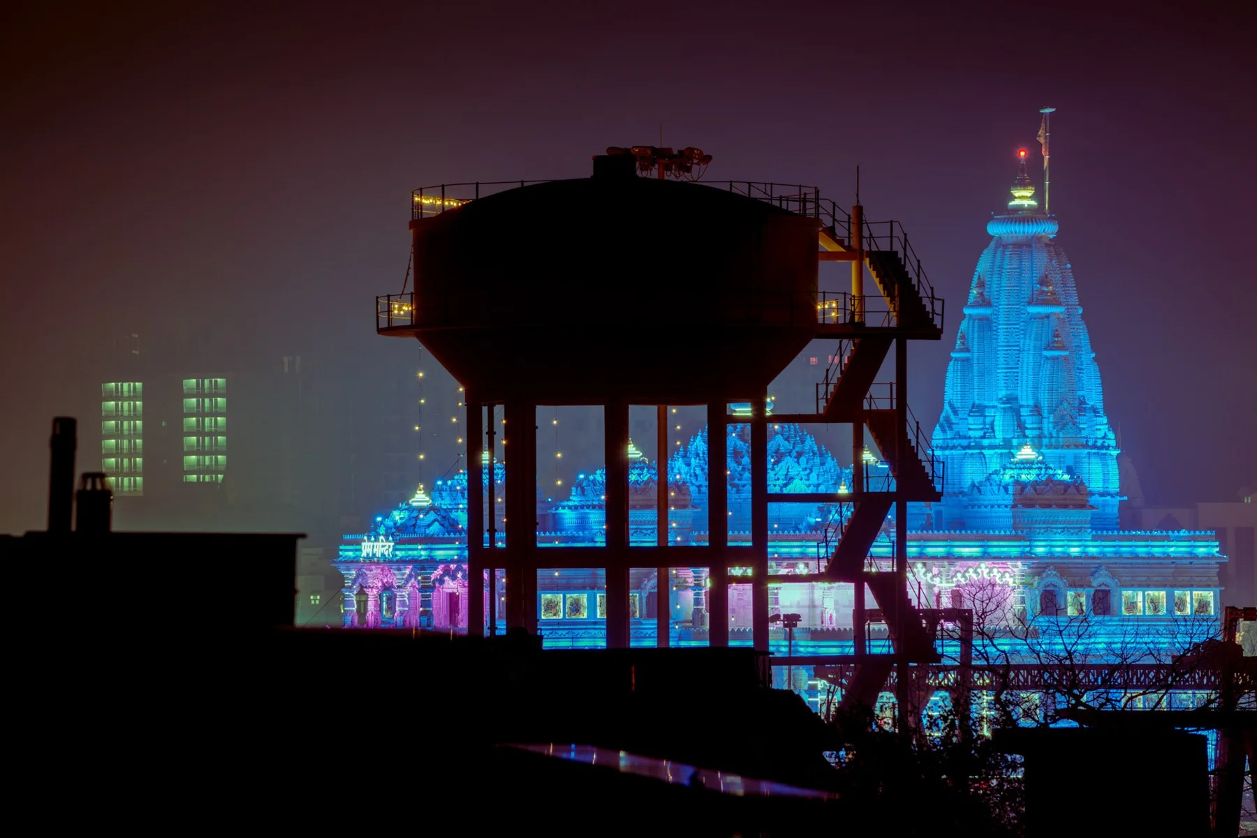 Night-time fine art photograph of a water tower silhouetted against illuminated skyscrapers