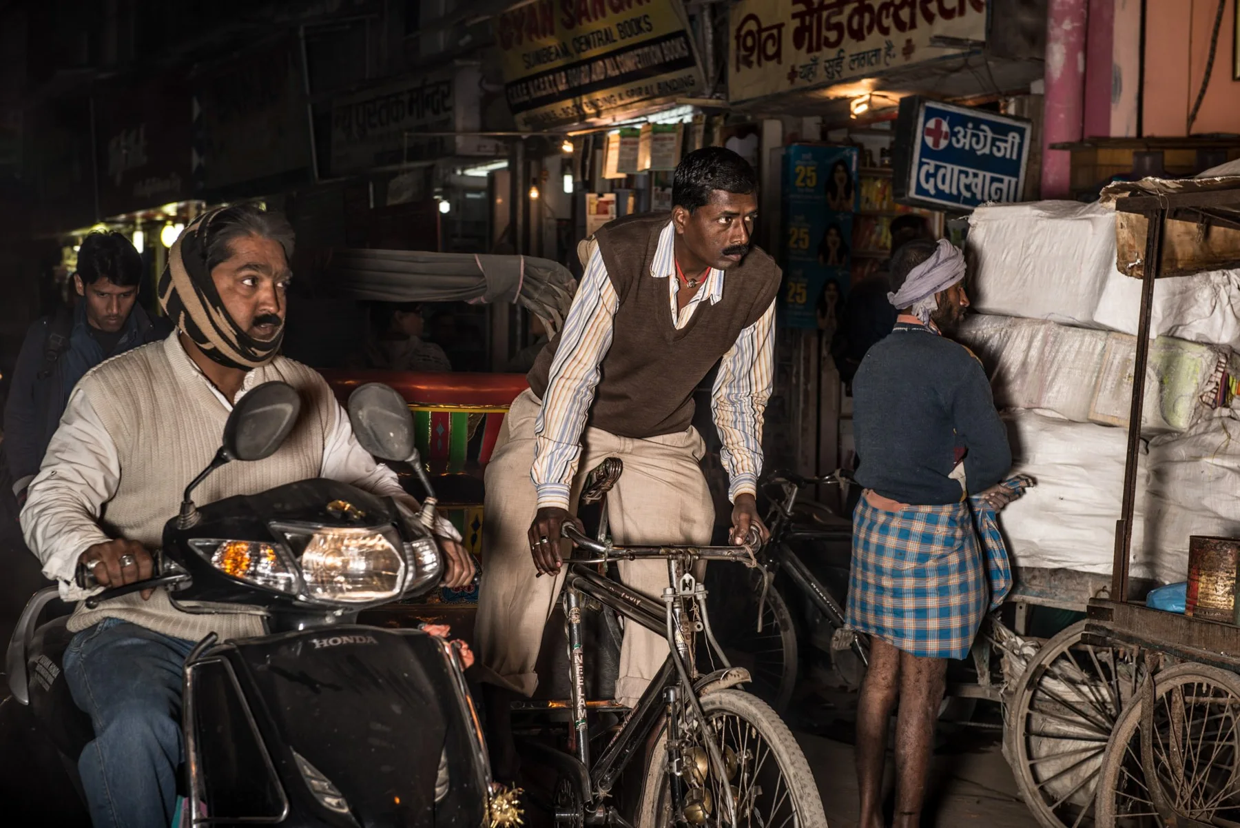 Nocturnal street scene with scooter riders, bicycle and market stalls.