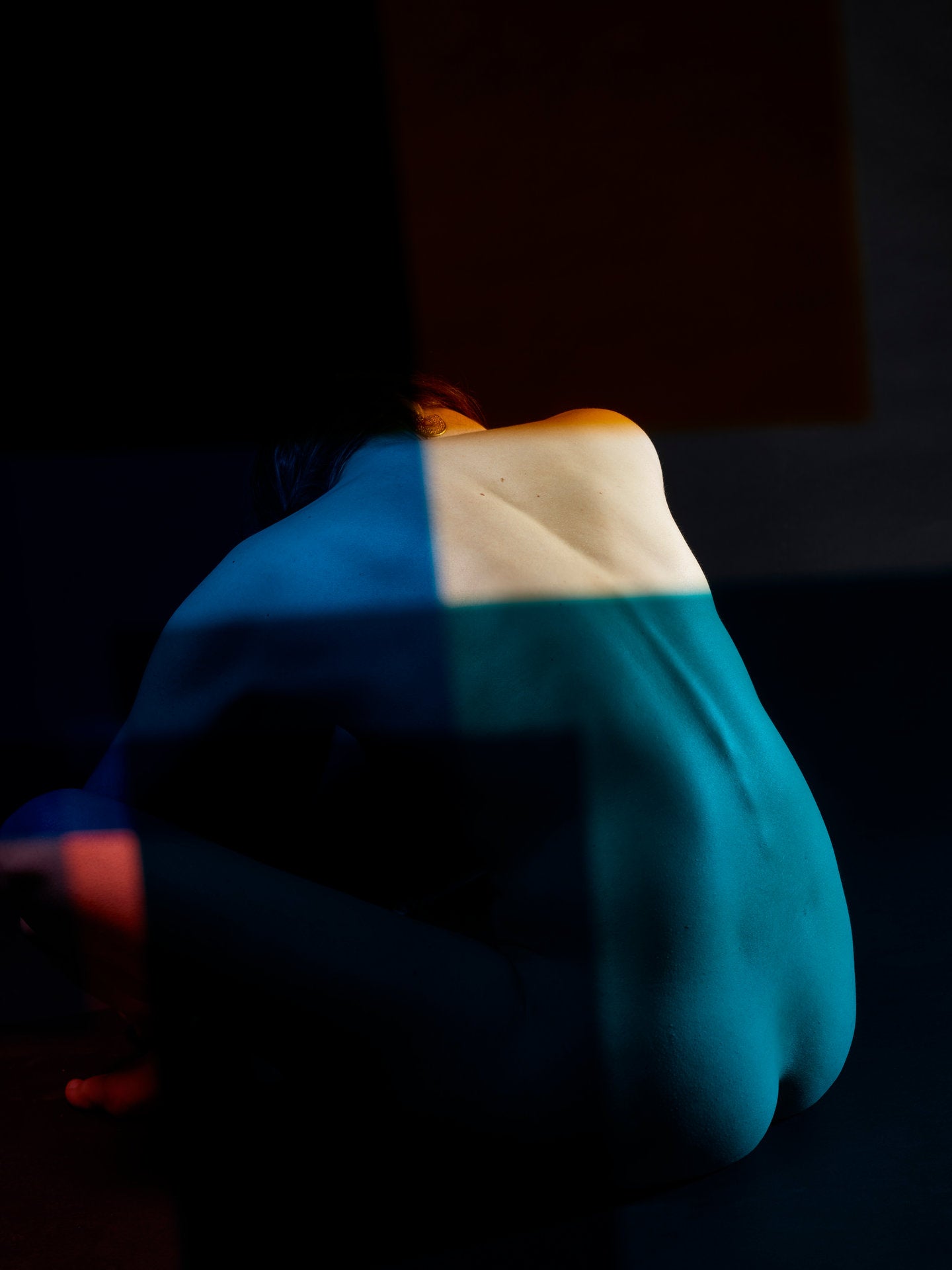 Fine art photography by André Wagner: A tightly gathered seated figure appears against near-black ground — Paula XIII.