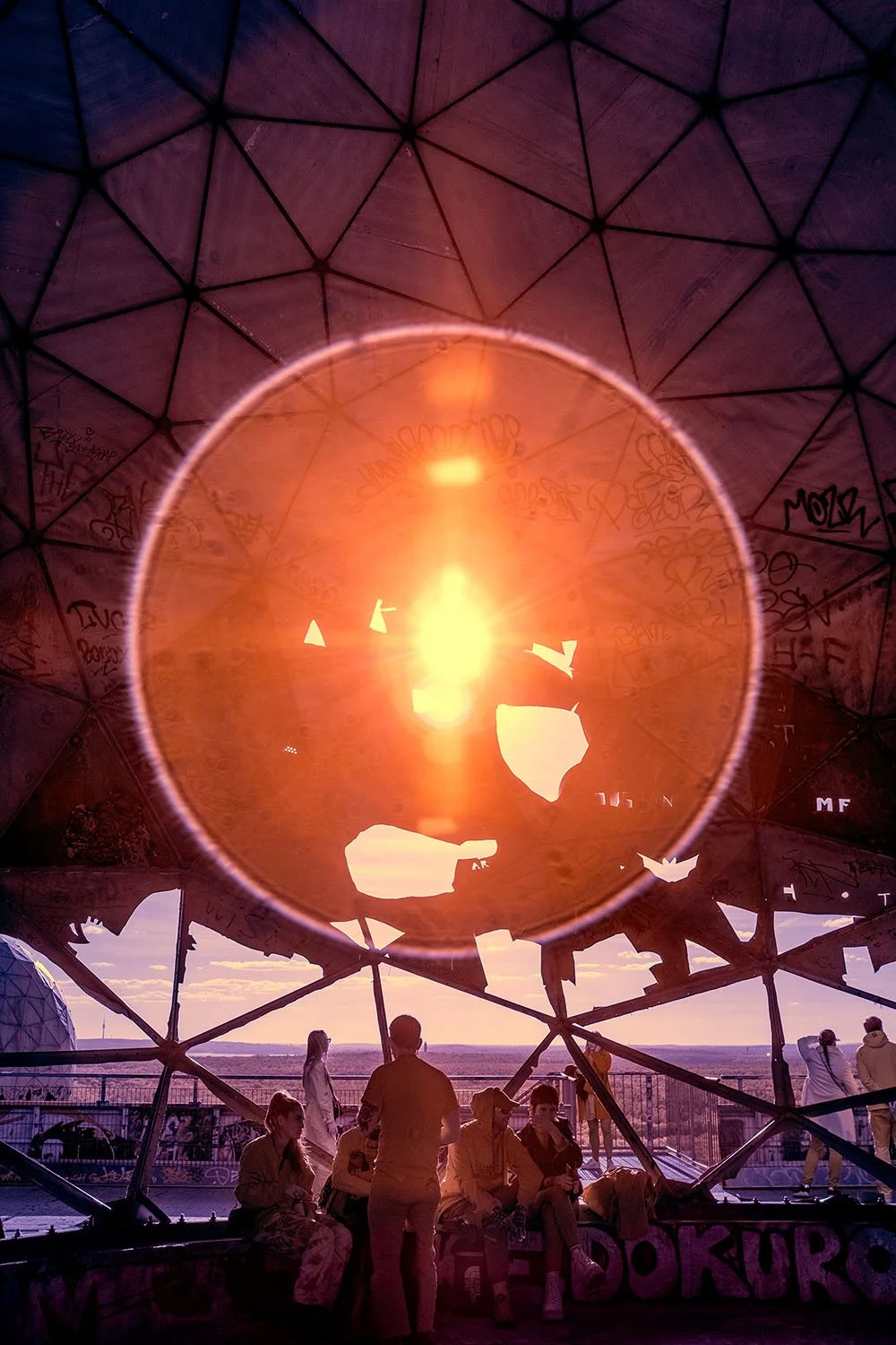 Group of people at sunset in the radar station Teufelsberg Berlin – art photography by André Wagner, taken through the broken dome with an intense circle of light