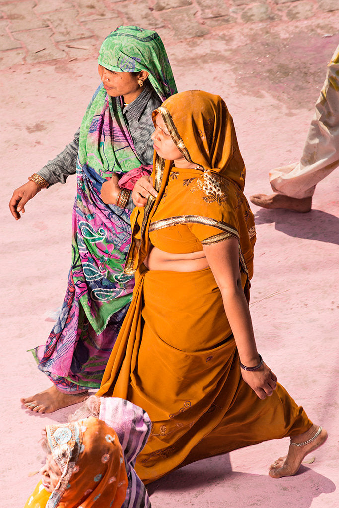 Fine art photography by André Wagner: Two women walk together in strongly contrasting garments: warm orange in front, green and pink pattern behind — Pilgrim on Purple Dust 6, Indien.