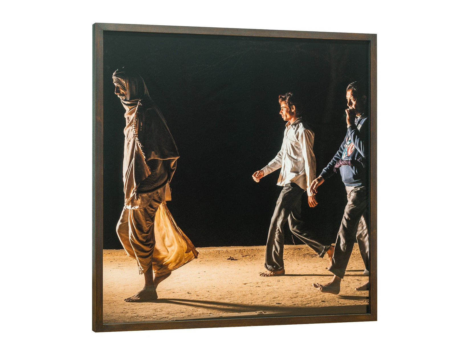 Photographie d’art d’André Wagner: Trois personnes traversent un chemin éclairé d’une lumière chaude sur un fond presque noir — Pilgrims at govardhan 10, Indien.