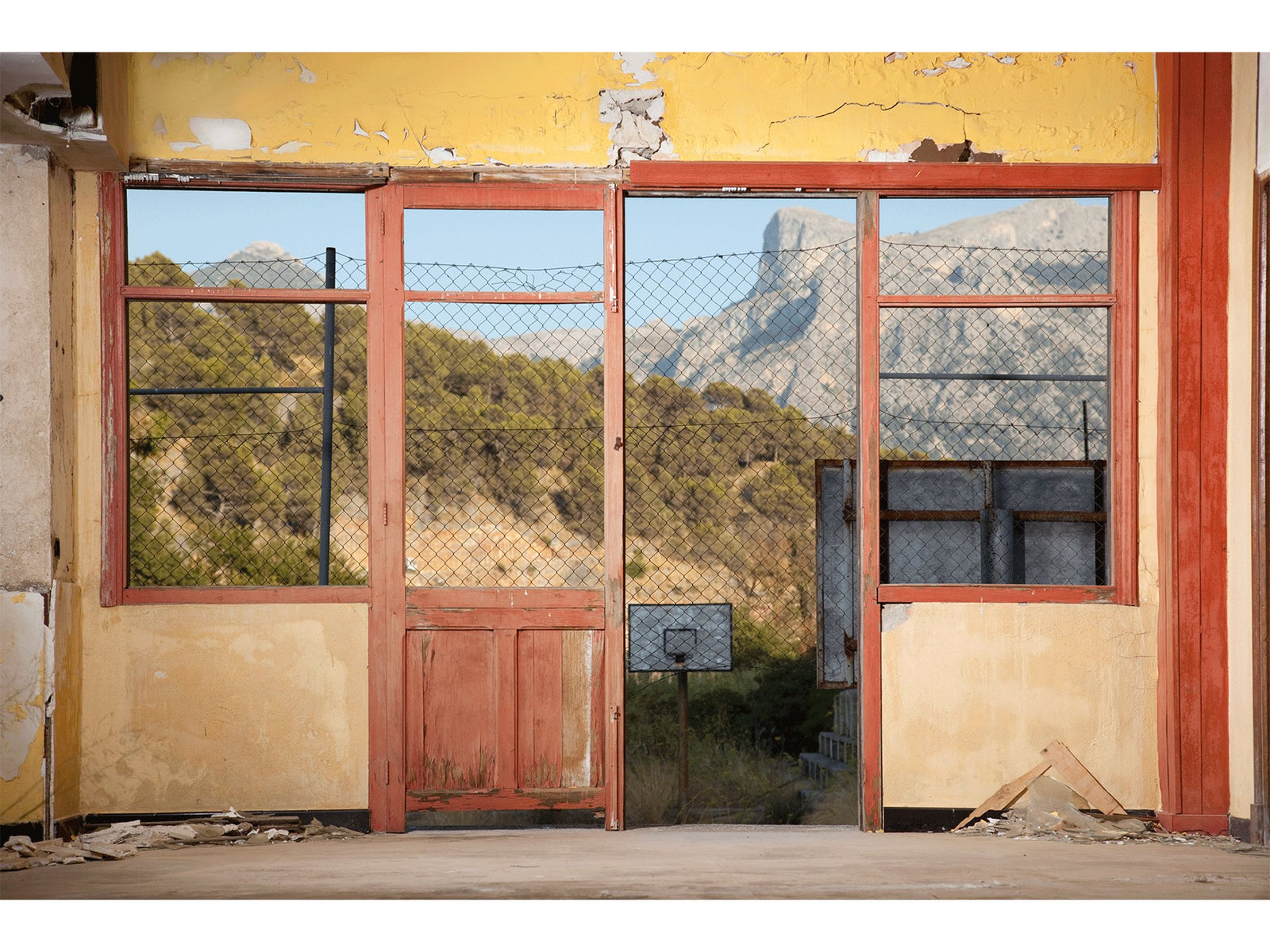 Fine art photography by André Wagner: A damaged yellow wall surrounds a red door and large window openings — Salon - old hotel, Spanien.