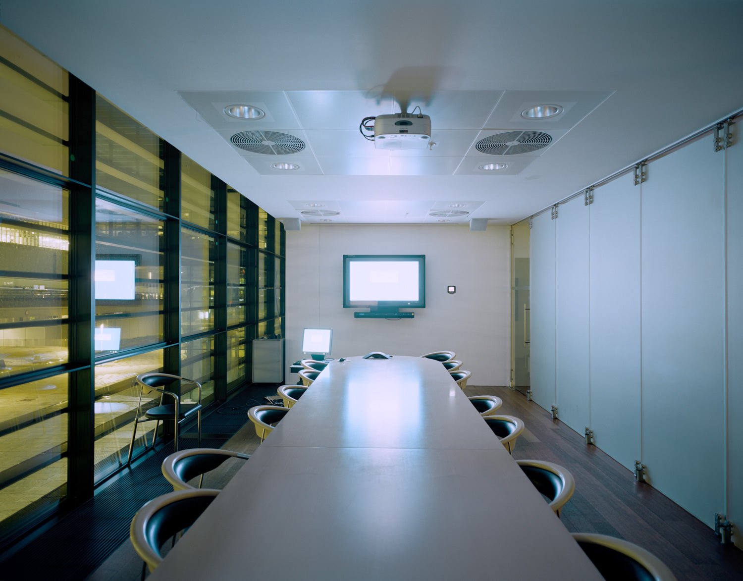 Fine art photography by André Wagner: A long meeting table leads between empty chairs towards a small screen — Secret Agent, Dänemark.