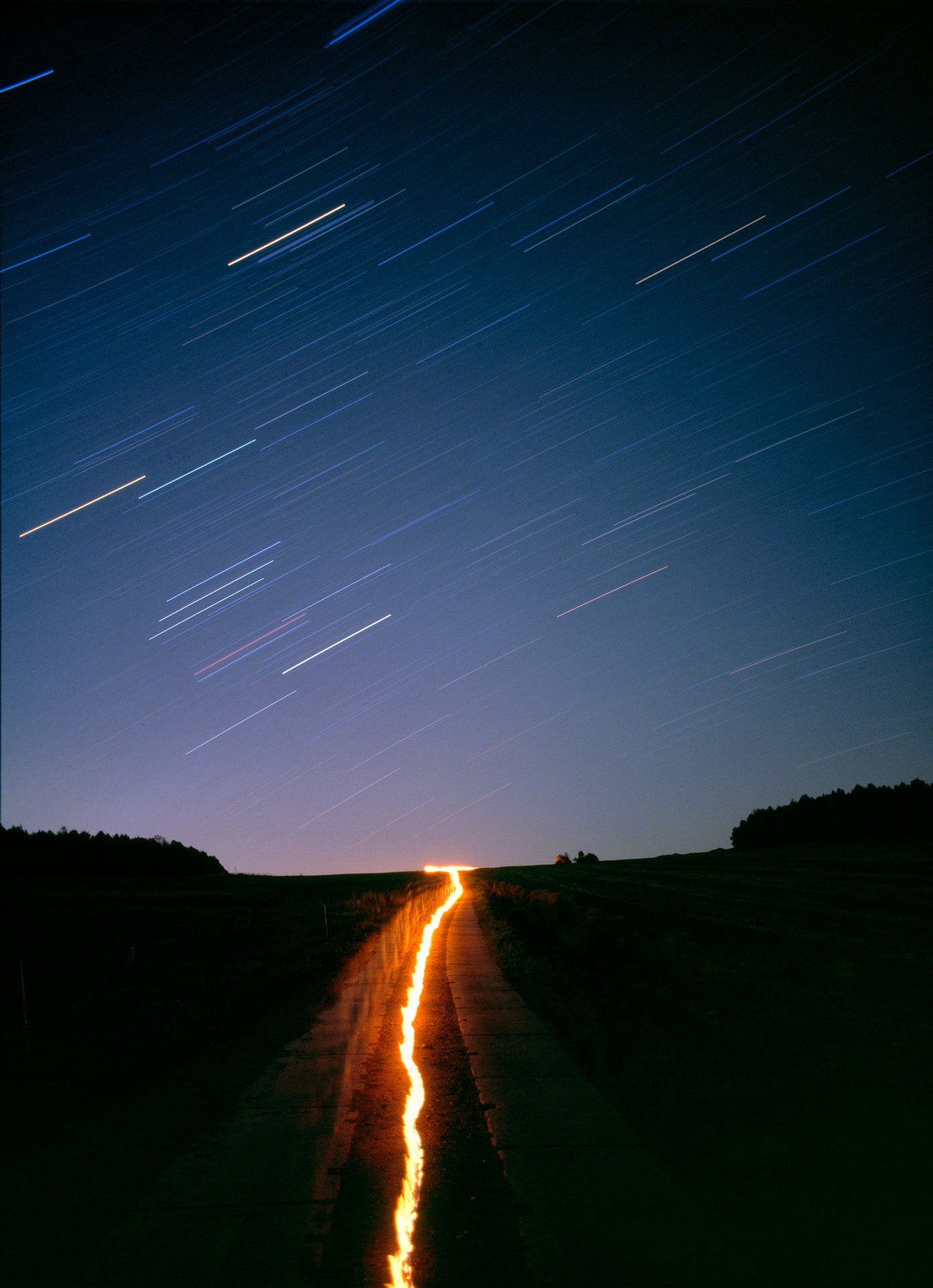Photographie d’art d’André Wagner: Une ligne incandescente part du bord inférieur et traverse le paysage sombre jusqu’à l’horizon plat — Star Walk 2.