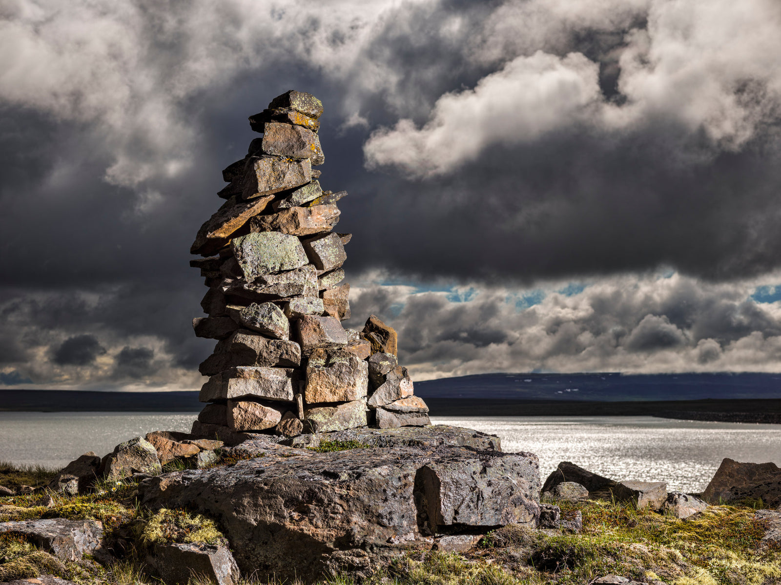 Photographie d’art d’André Wagner: Un empilement irrégulier de pierres s’élève au-dessus de grands rochers plats — Stoneman 2, Island.