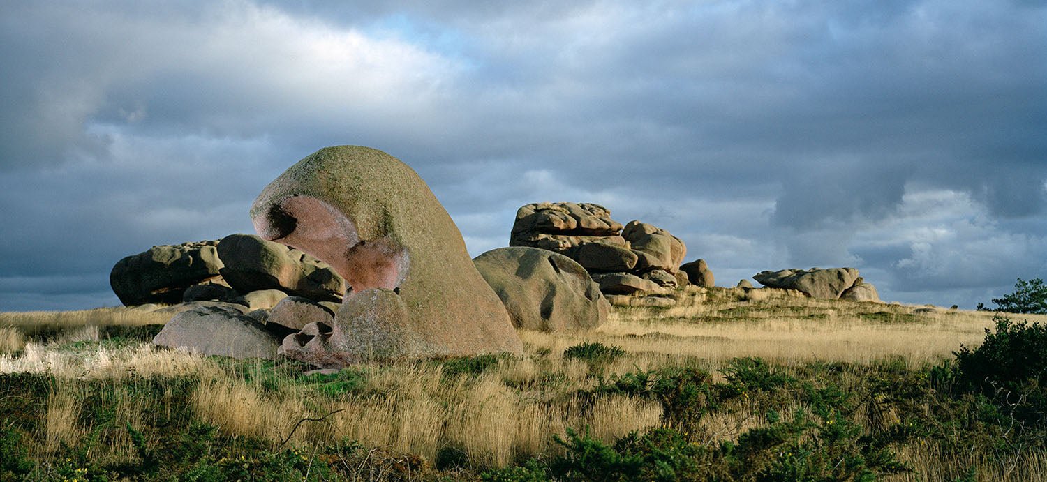 Fine art photography by André Wagner: A large rounded rock stands among smaller stones in low grassland — Story of wind 2, Frankreich.