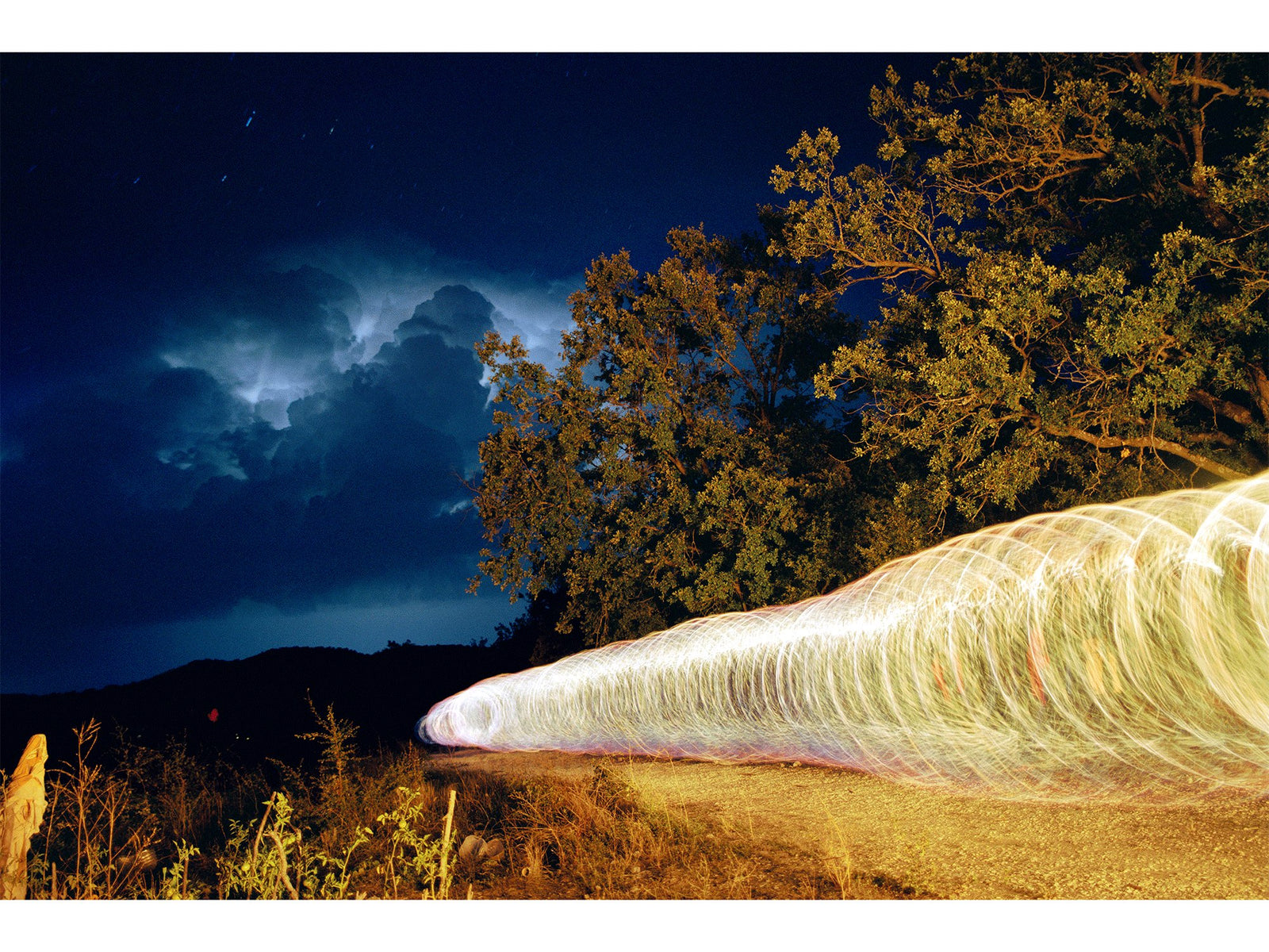 Fine art photography by André Wagner: A broad sequence of bright loops crosses the night landscape diagonally from the right — Swing, Spanien.