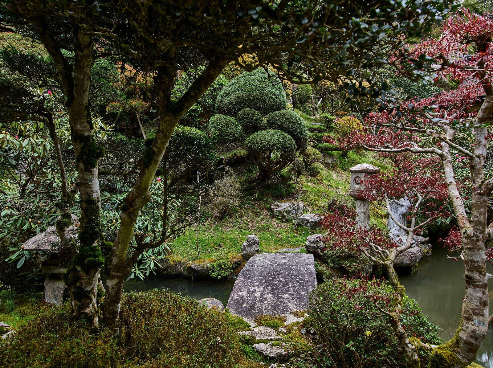 Photographie d’art d’André Wagner: Entre les arbres, un petit pont de pierre traverse une eau sombre — Temple in oku-no, Japan.