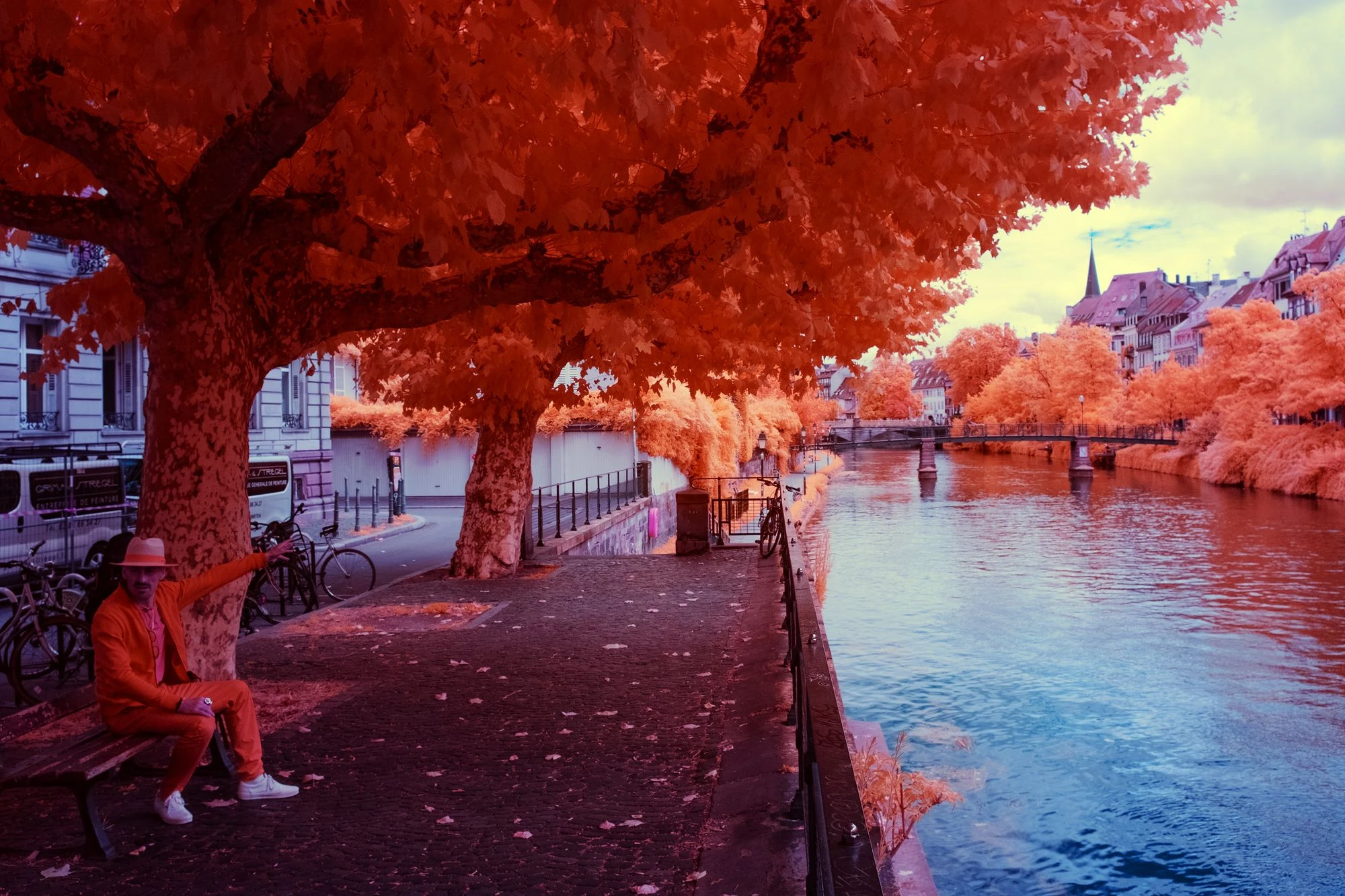 Photographie d’art infrarouge d’André Wagner: Une personne est assise sous un large couvert orangé, au bord d’un chemin qui longe l’eau — The Orange Guide – Strasbourg.
